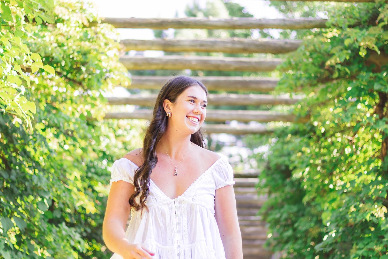 A white summer dress photographed in a lush garden setting with natural sunlight filtering through trees.