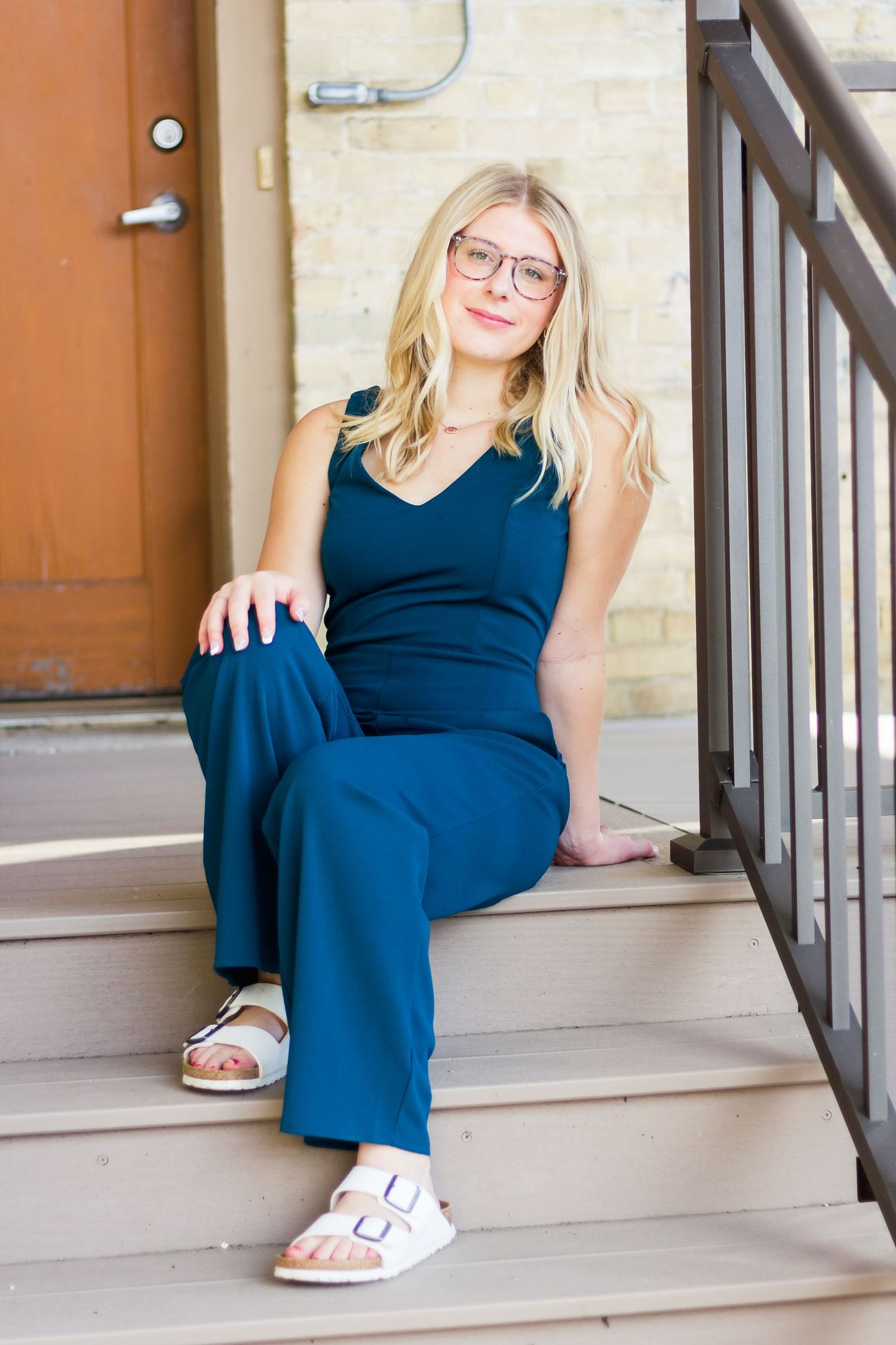 Woman in navy jumpsuit and sandals sits casually on concrete steps.