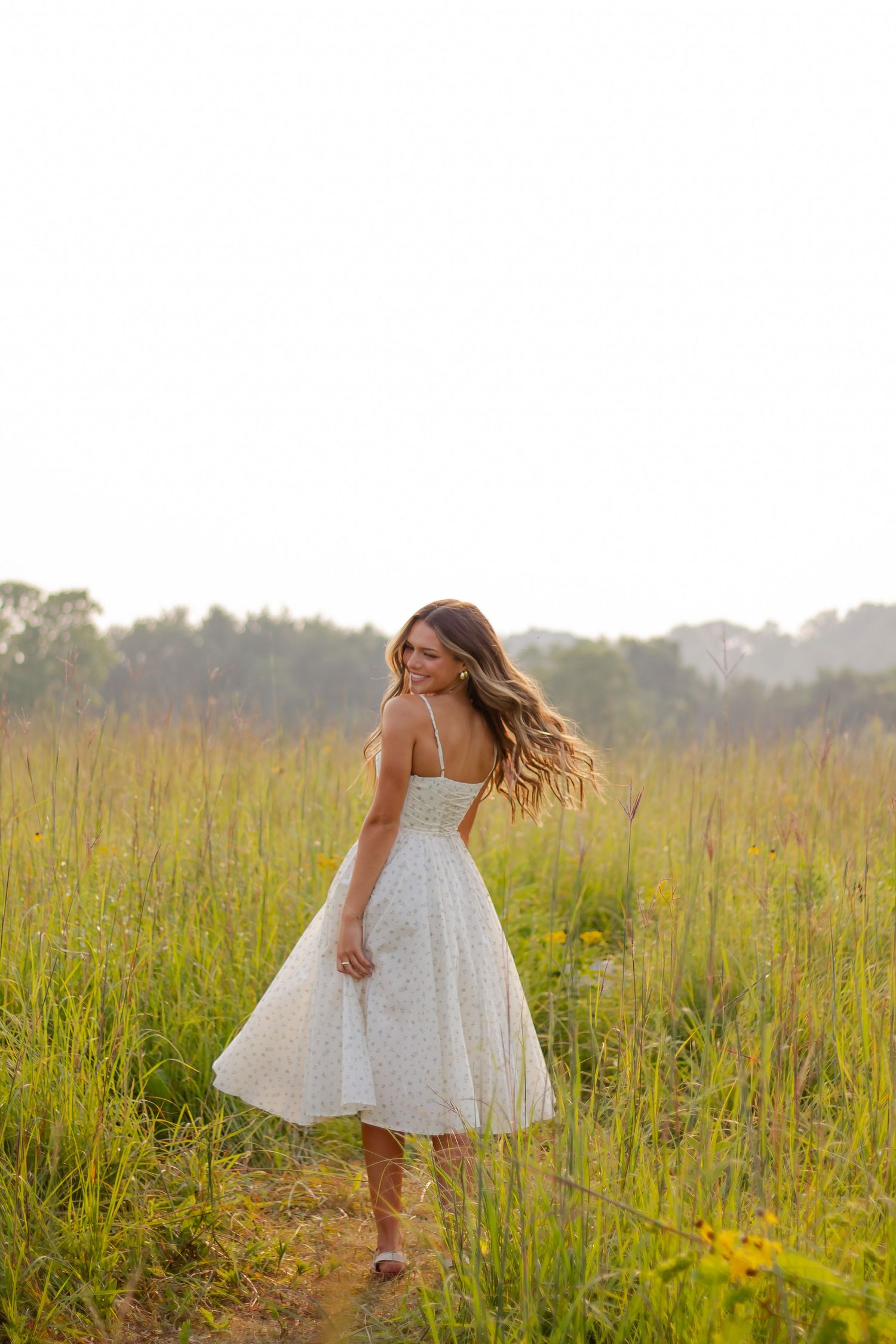 Woman in white dress twirling in sunlit meadow with tall grass.