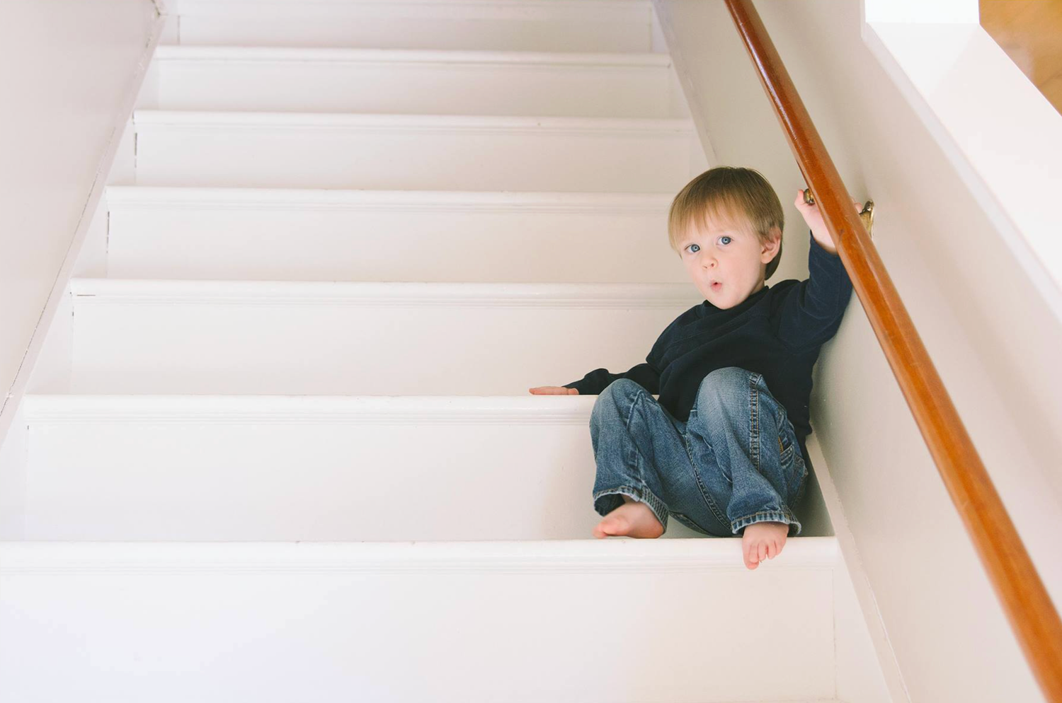 Small child sitting on white carpeted stairs next to wooden banister.