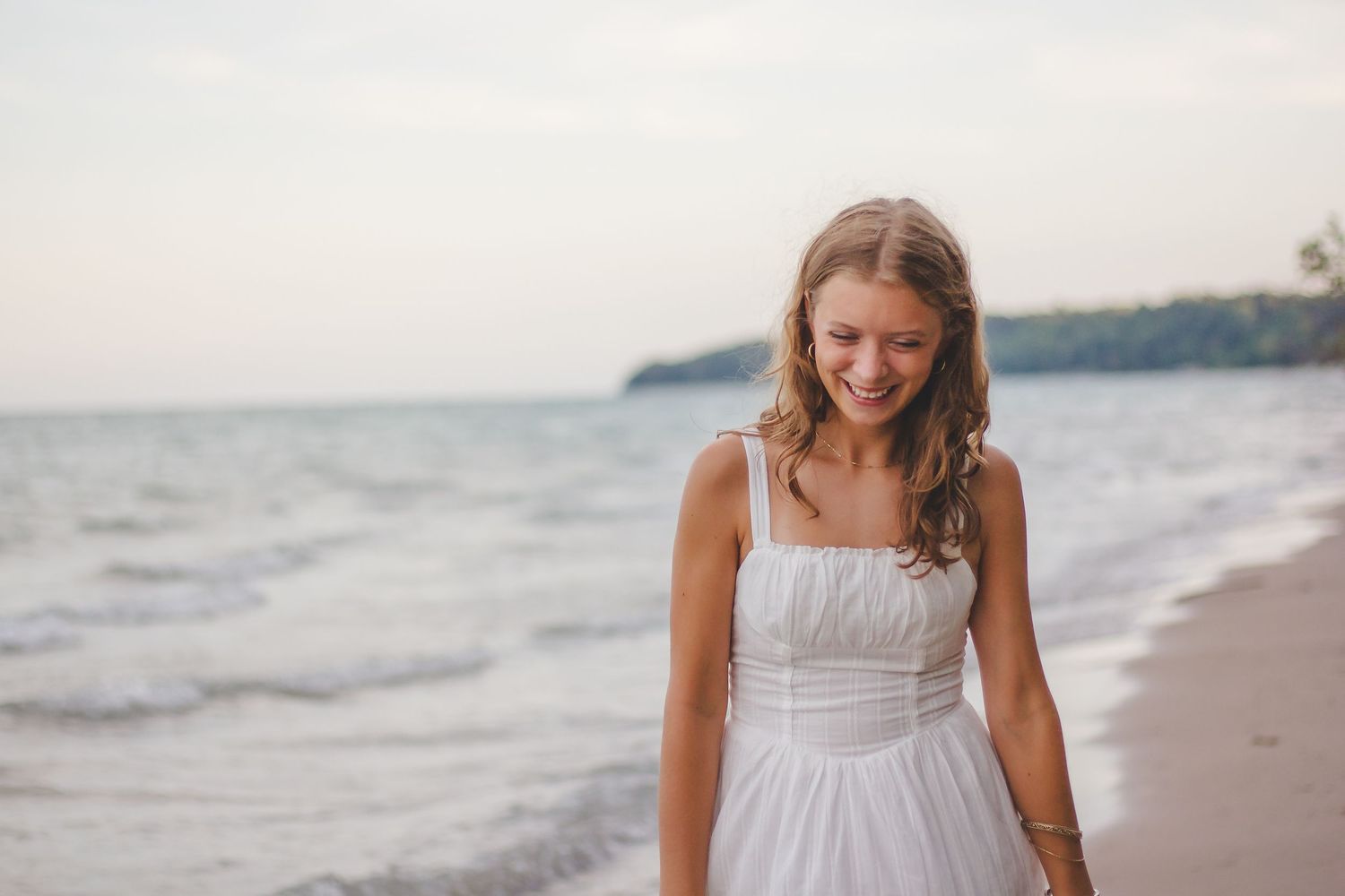 Woman in white sundress smiling on a beach at sunset.