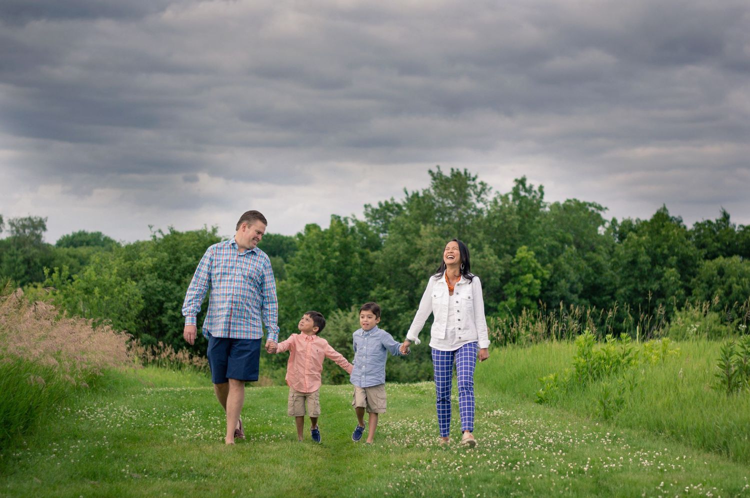 Family walking together through a green meadow under cloudy skies.