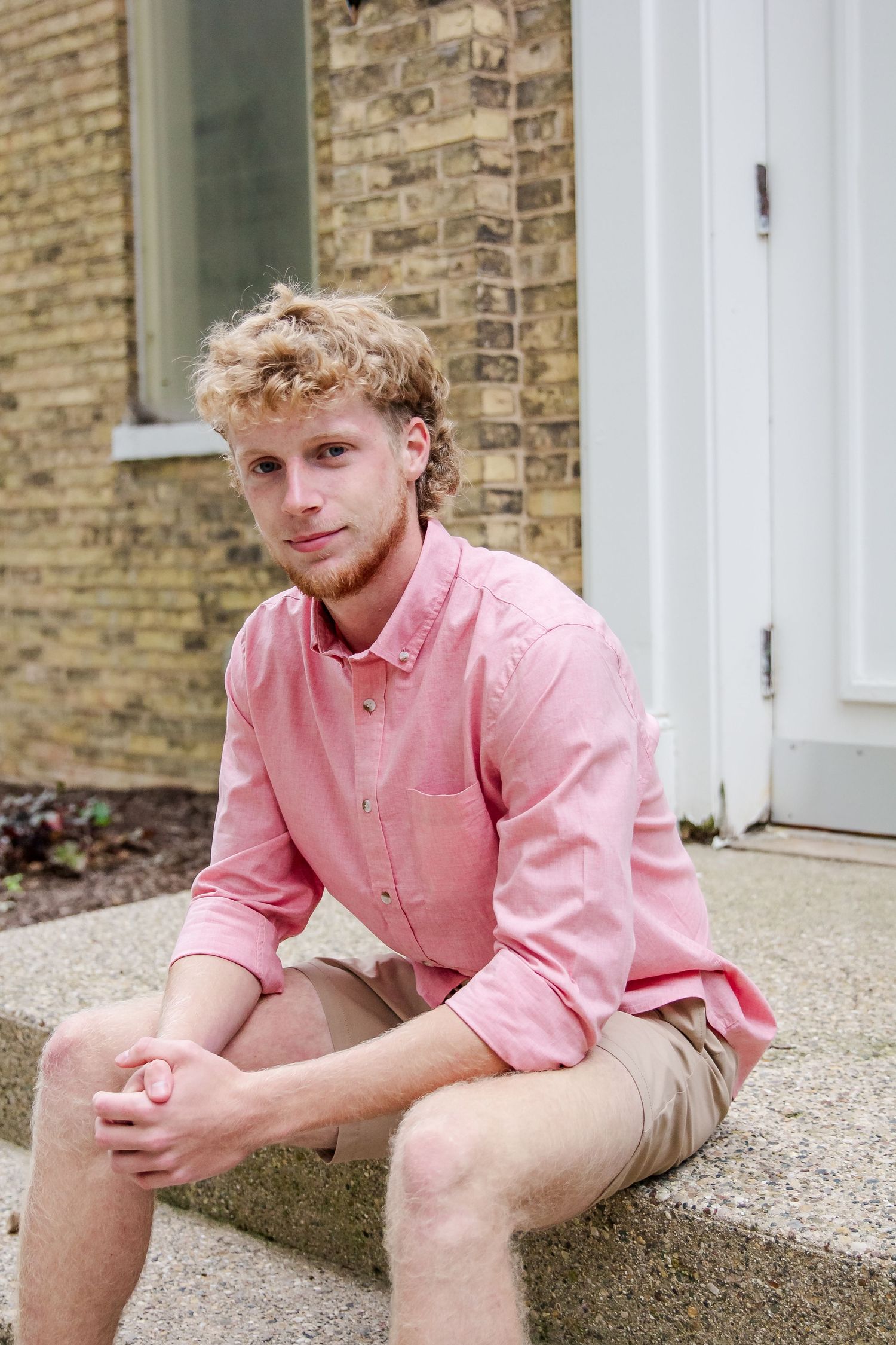 Student in pink button-down shirt sits casually on stone steps.