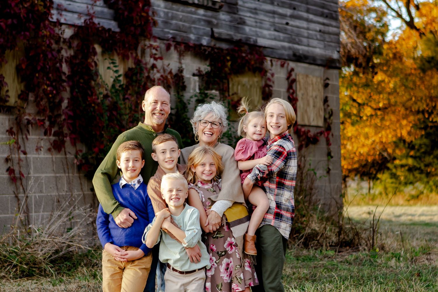 Grandparents pose with their grands outdoors in autumn with colorful fall foliage and trees in the background at at Oconomowoc photo session