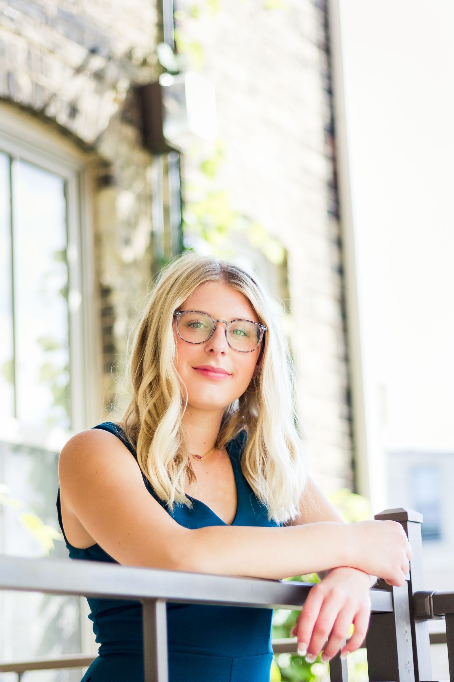 Portrait of woman in navy dress leaning on railing in sunlit architectural setting.