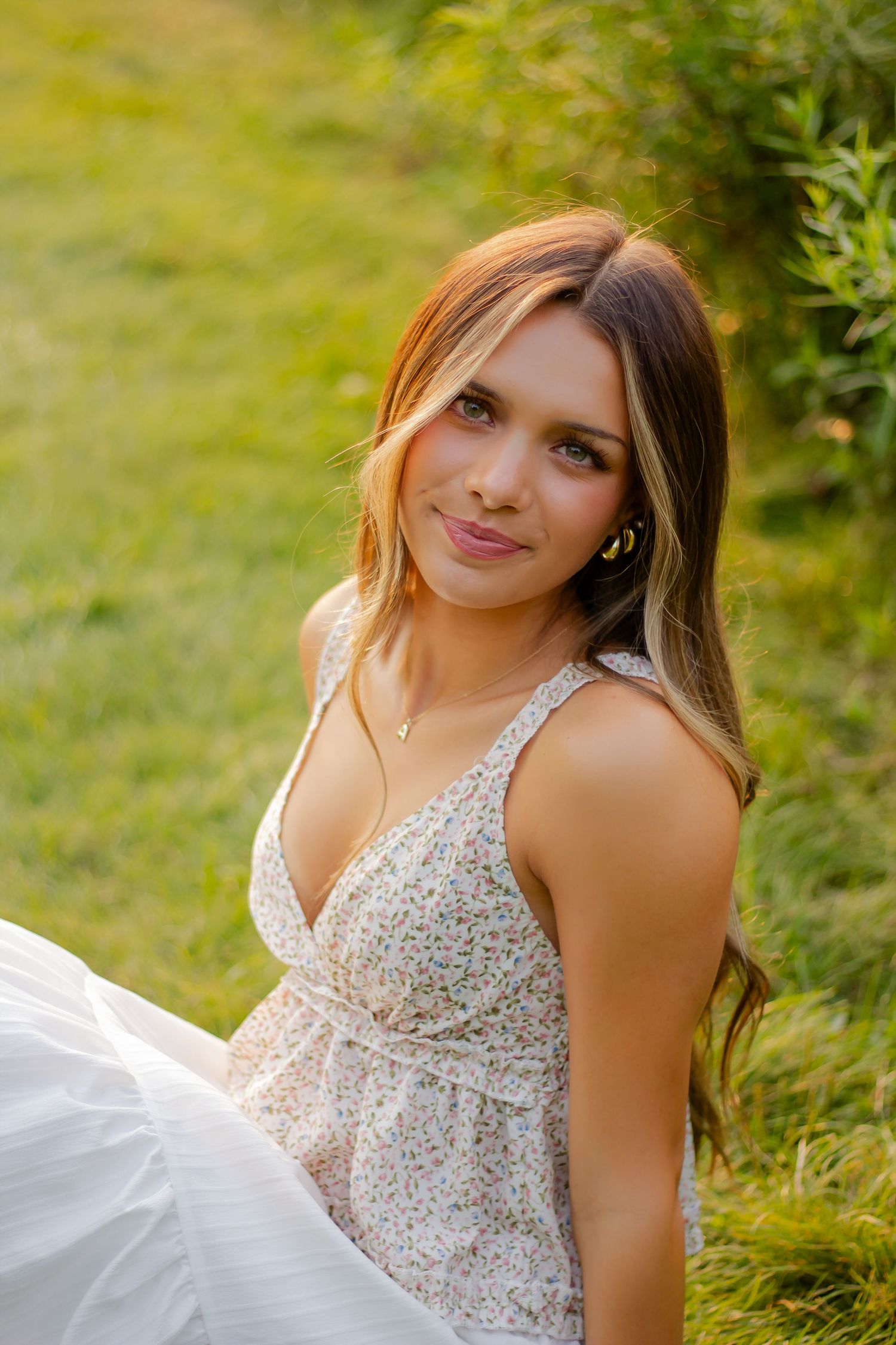Woman in white floral dress sitting in sunny meadow during golden hour.