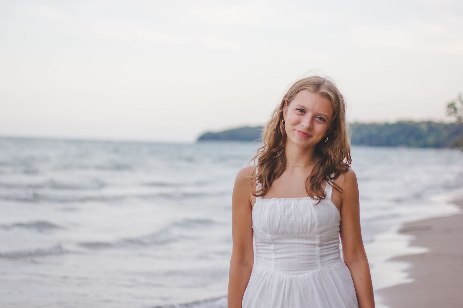 Person in white dress walking along misty beach shoreline.