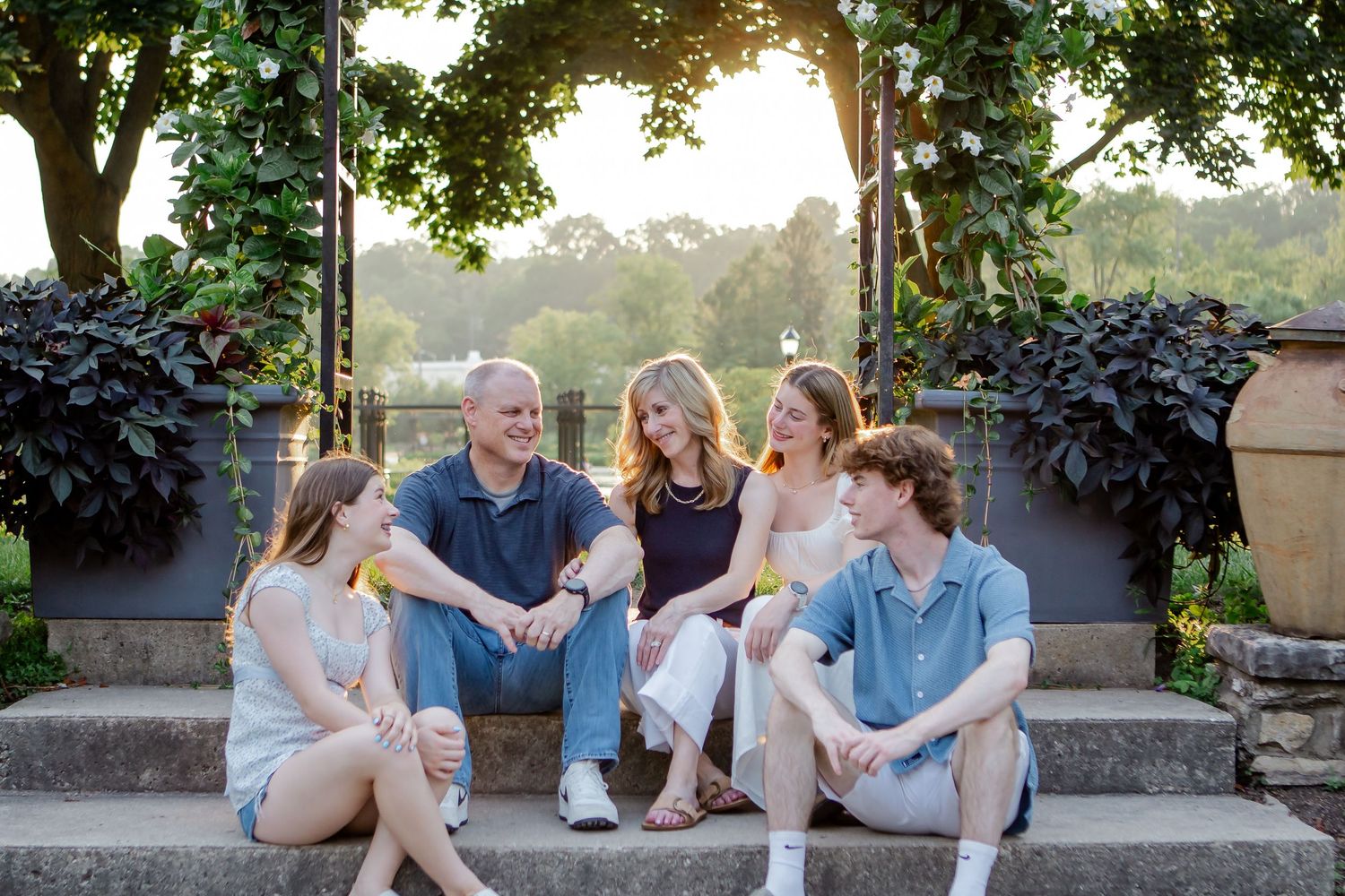 Family relaxing together on stone wall in garden setting.
