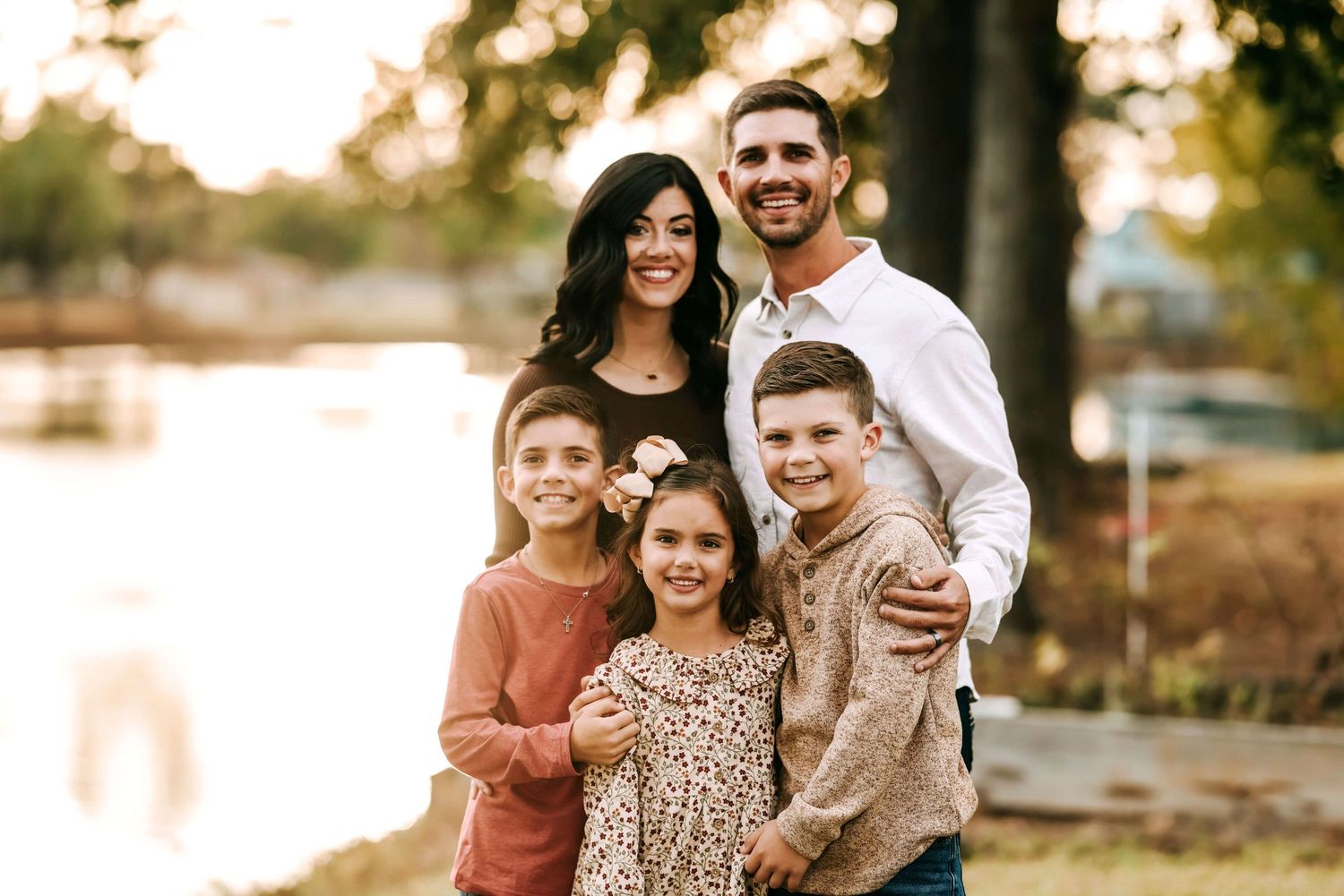 Family of four posing together outdoors at sunset with a lake in the background.
