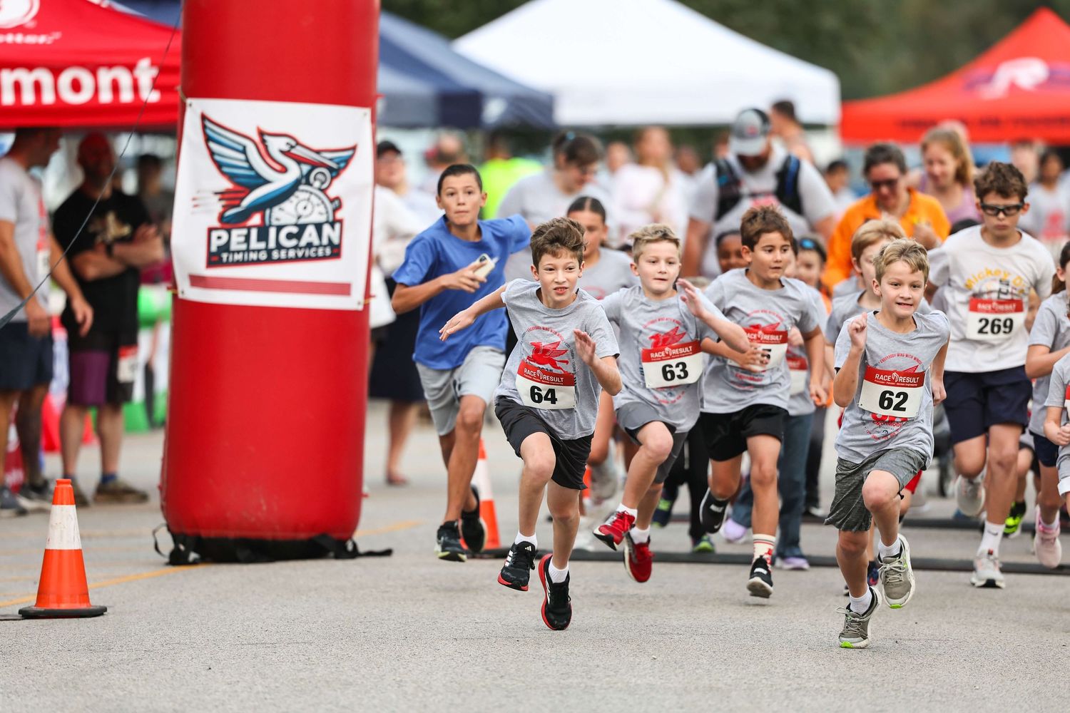 Runners compete in a race with red banners and tents visible along the course during an outdoor event.