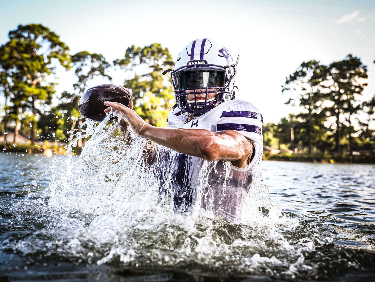 Football player in white uniform emerges from water with dramatic splash effect.