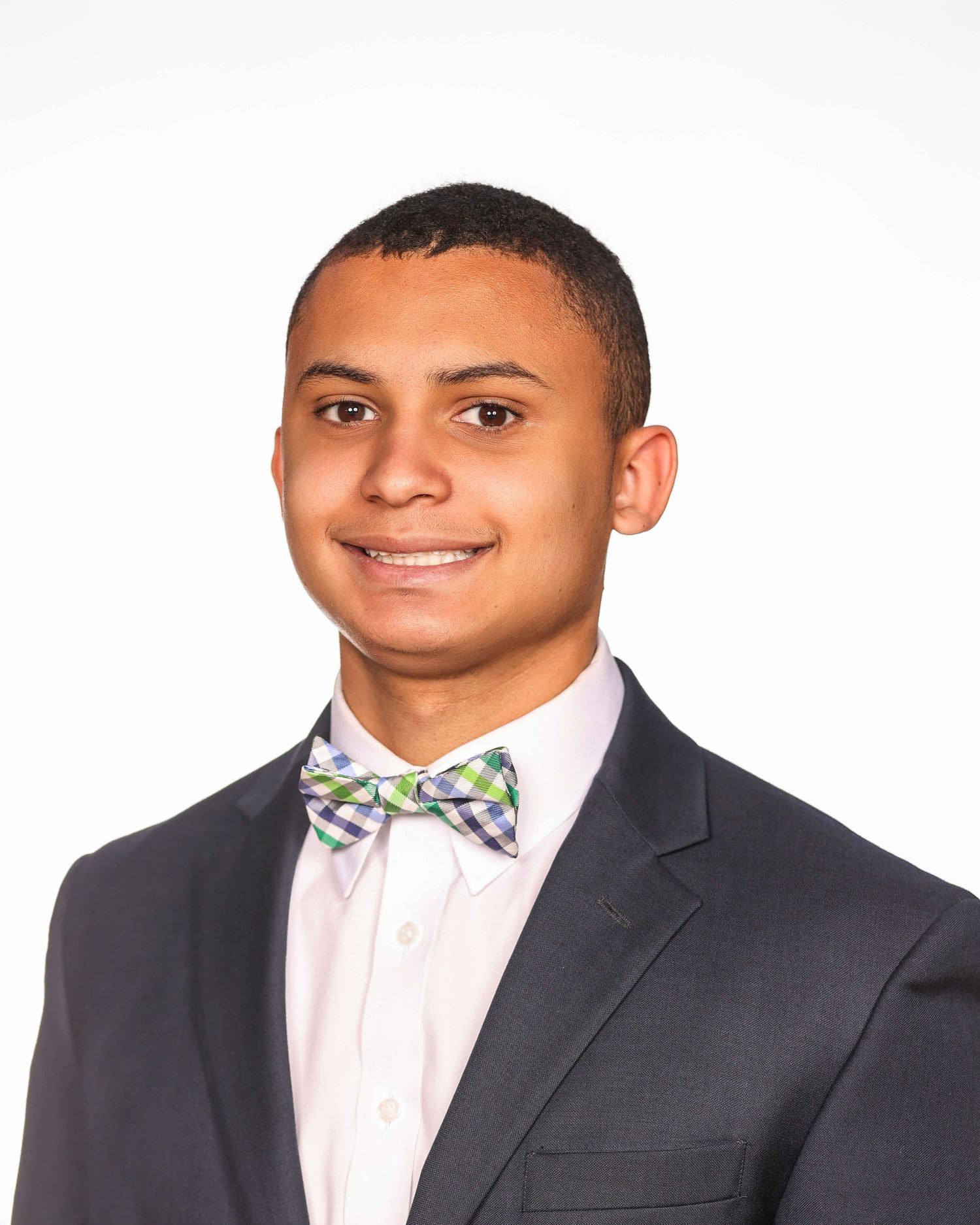 Professional headshot of a person in a gray suit and floral bow tie smiling warmly against a white background.