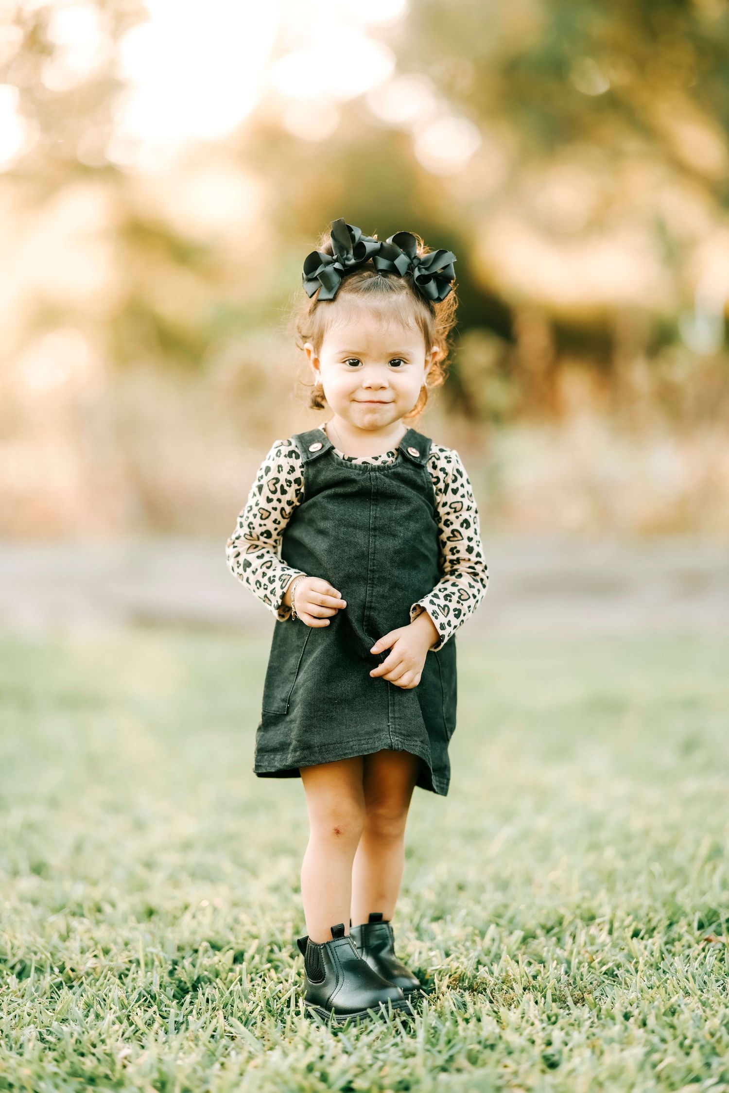 A small child in a black dress and leopard print top plays on green grass.