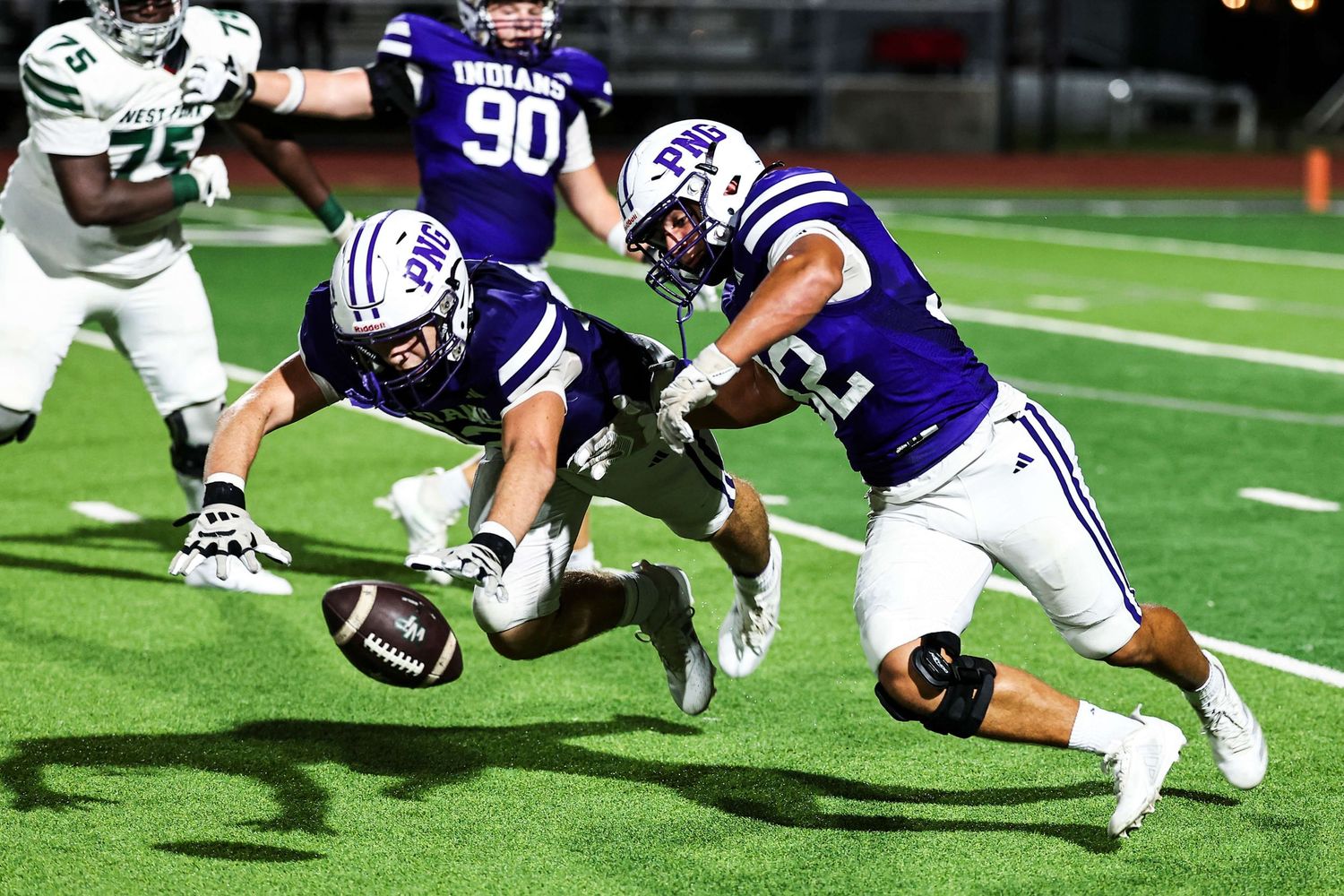Football players diving and tackling during a competitive play on the field.