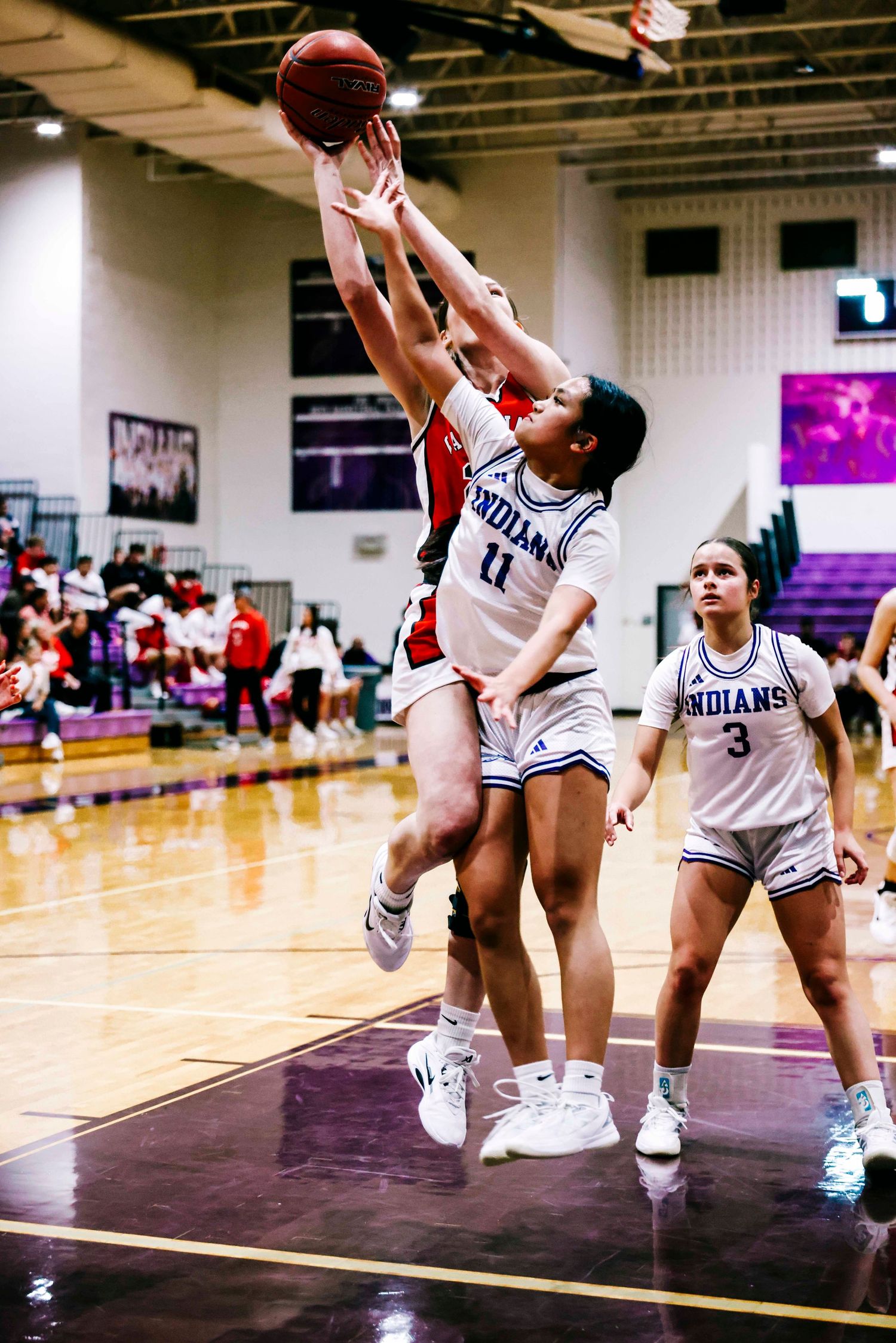 Basketball players jumping for the ball during an intense indoor game.