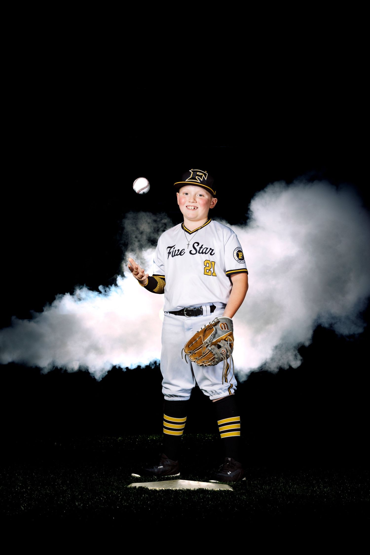 Baseball player in white uniform poses with ball and glove surrounded by dramatic smoke.