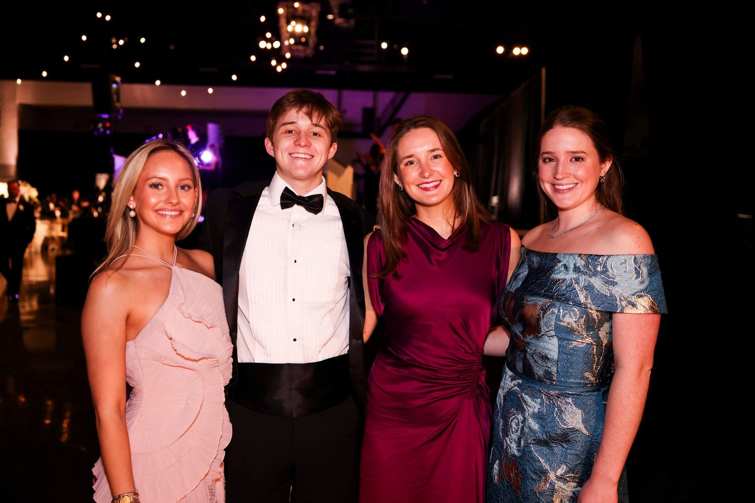 Group dressed in formal attire poses together at an elegant evening event with purple lighting.