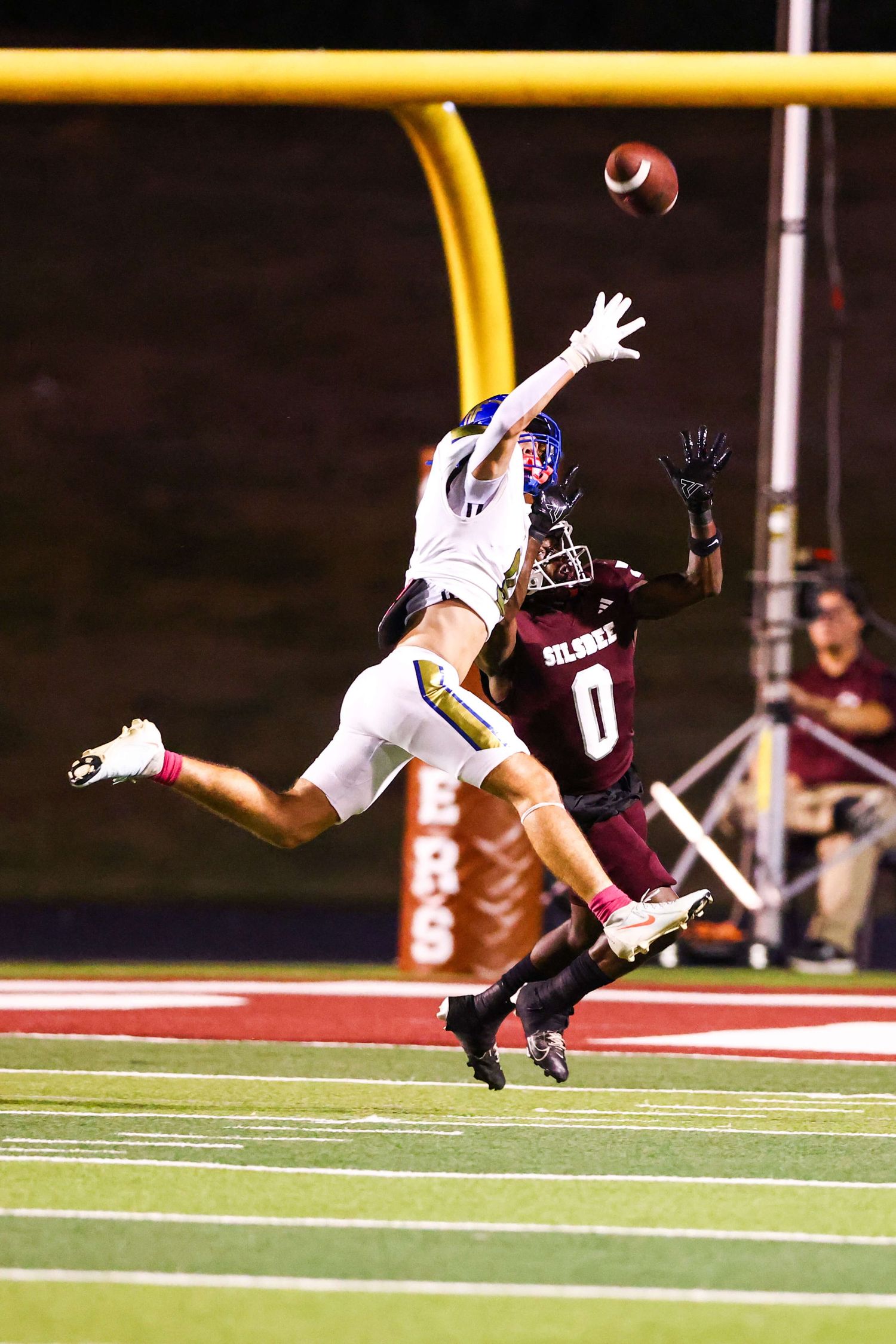 Football players leaping high to catch a pass during nighttime game.