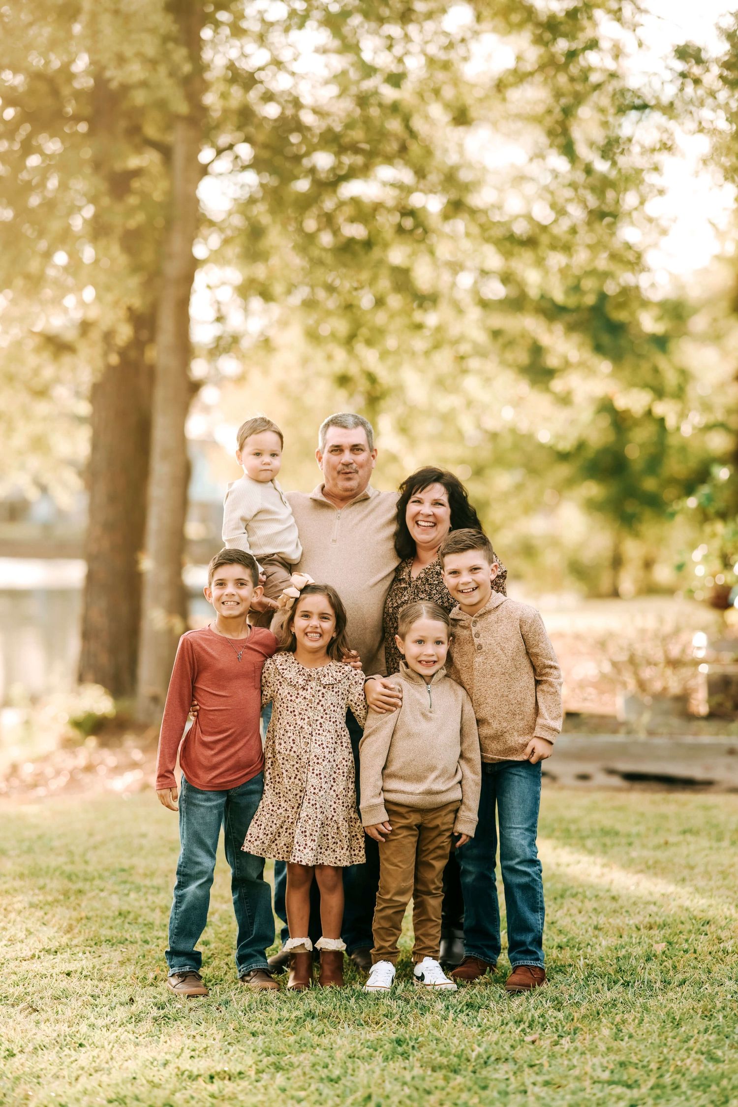A joyful outdoor family photo session with parents and children posing together on a grassy hill in autumn.