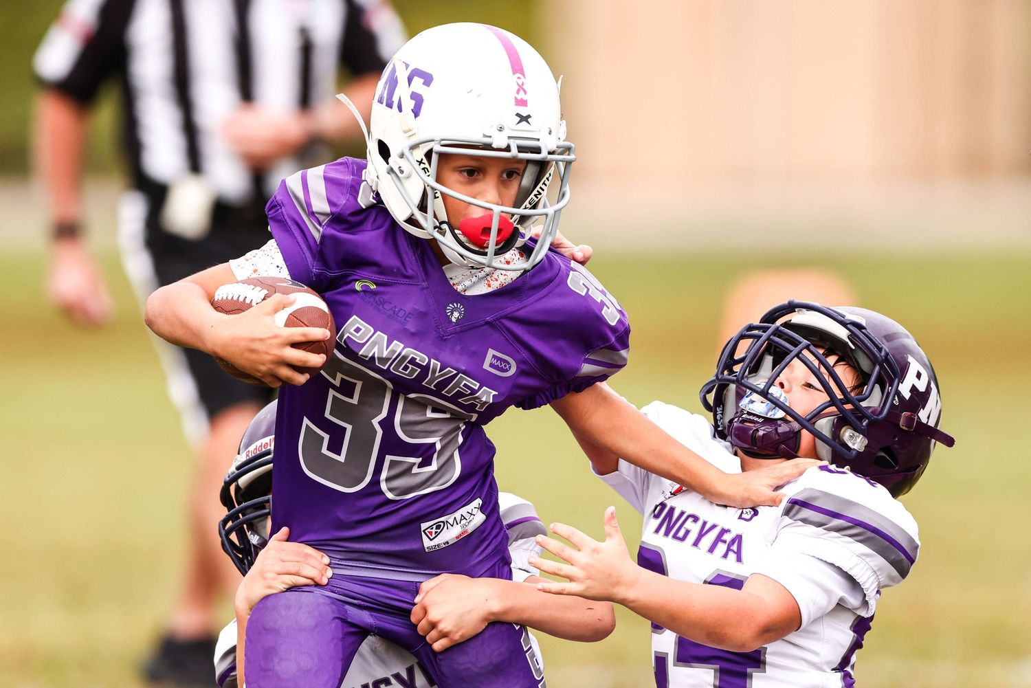 Youth football players in purple and white uniforms competing during tackle attempt.