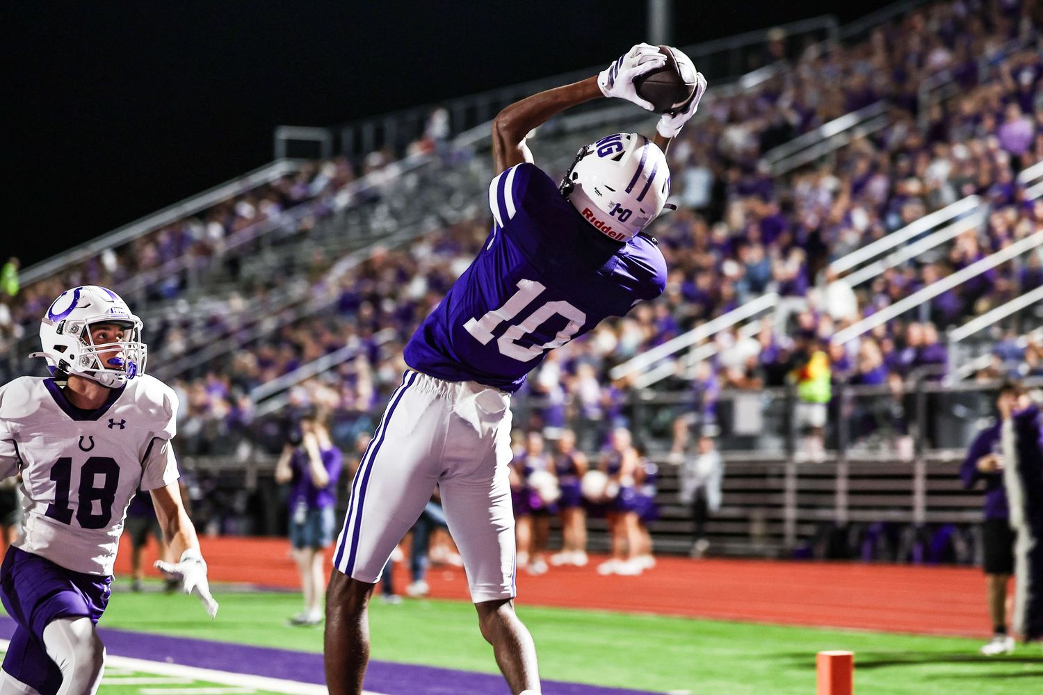 Athletes compete in a packed stadium during a nighttime football game.