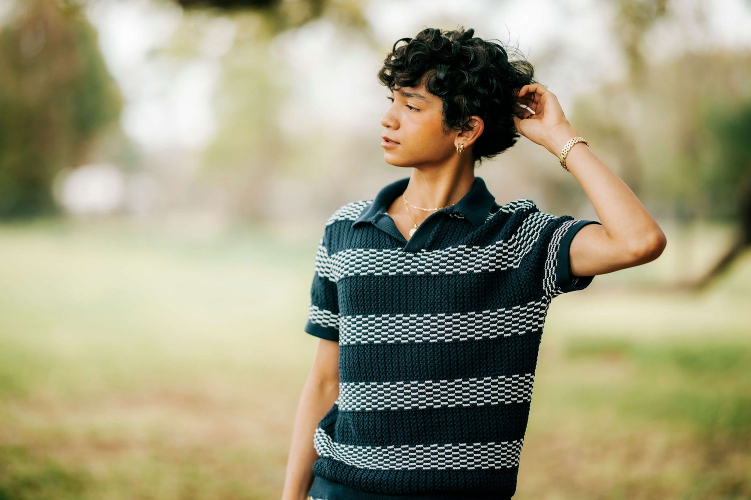 A person in a striped polo shirt poses casually outdoors with natural lighting.
