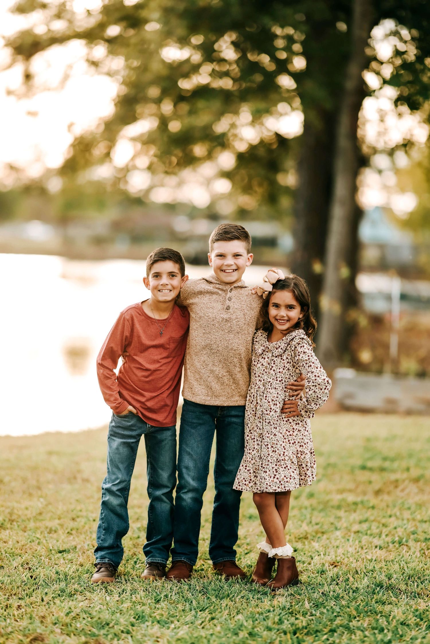 Three children stand together on grass during a sunny autumn afternoon.
