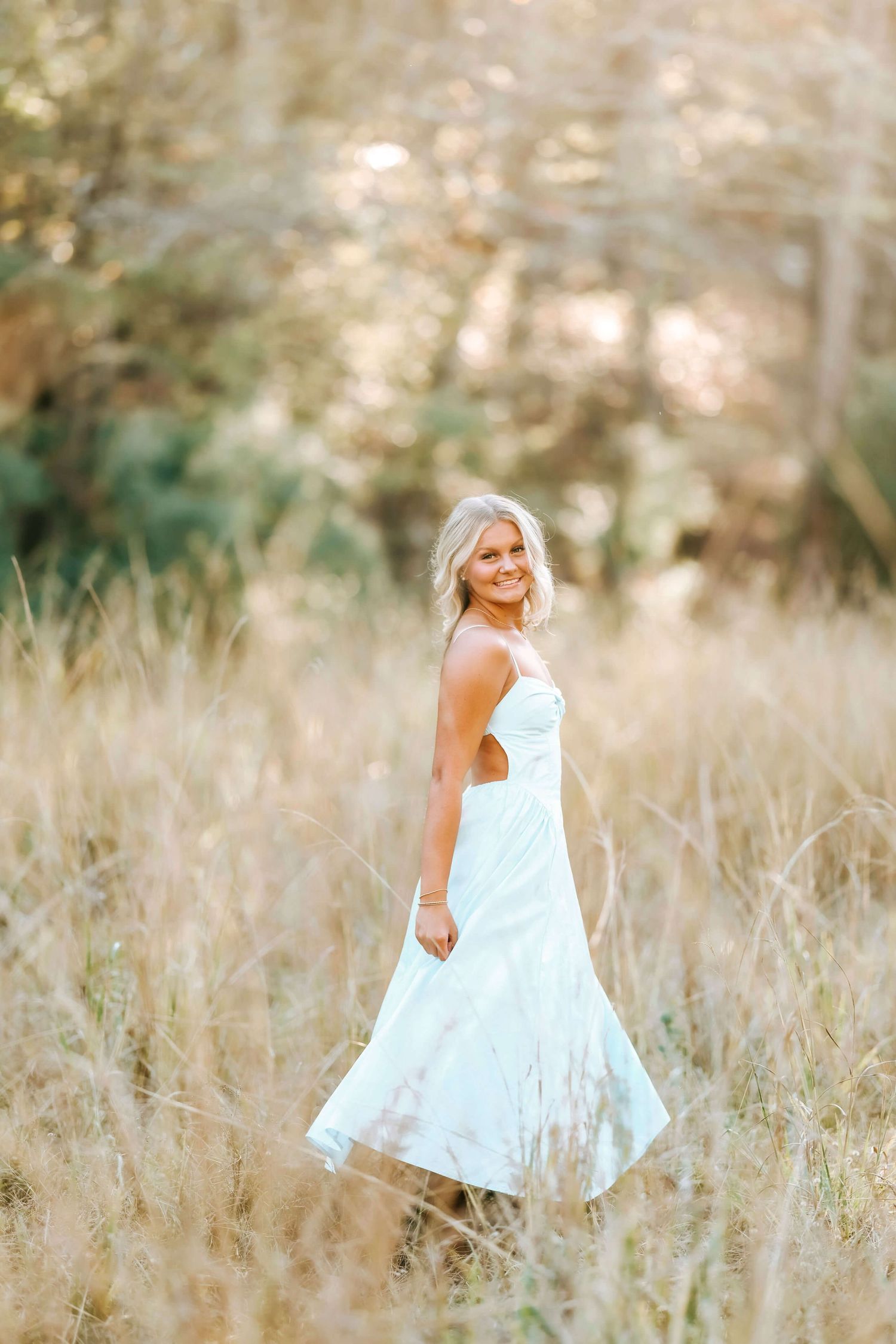 A person in a flowing white dress twirls in tall grass during golden hour.