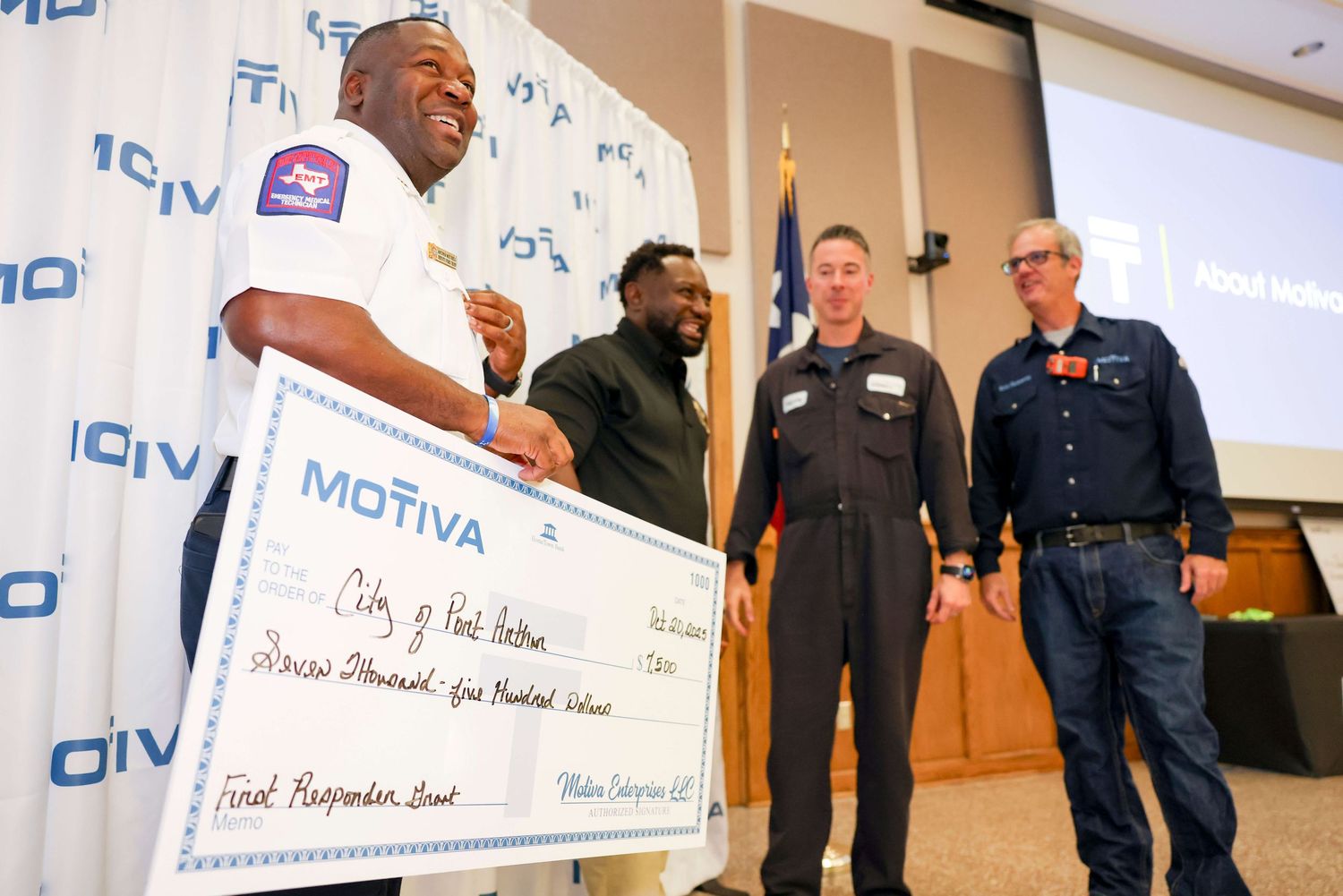 People gathered in a conference room holding large ceremonial checks at a presentation event.