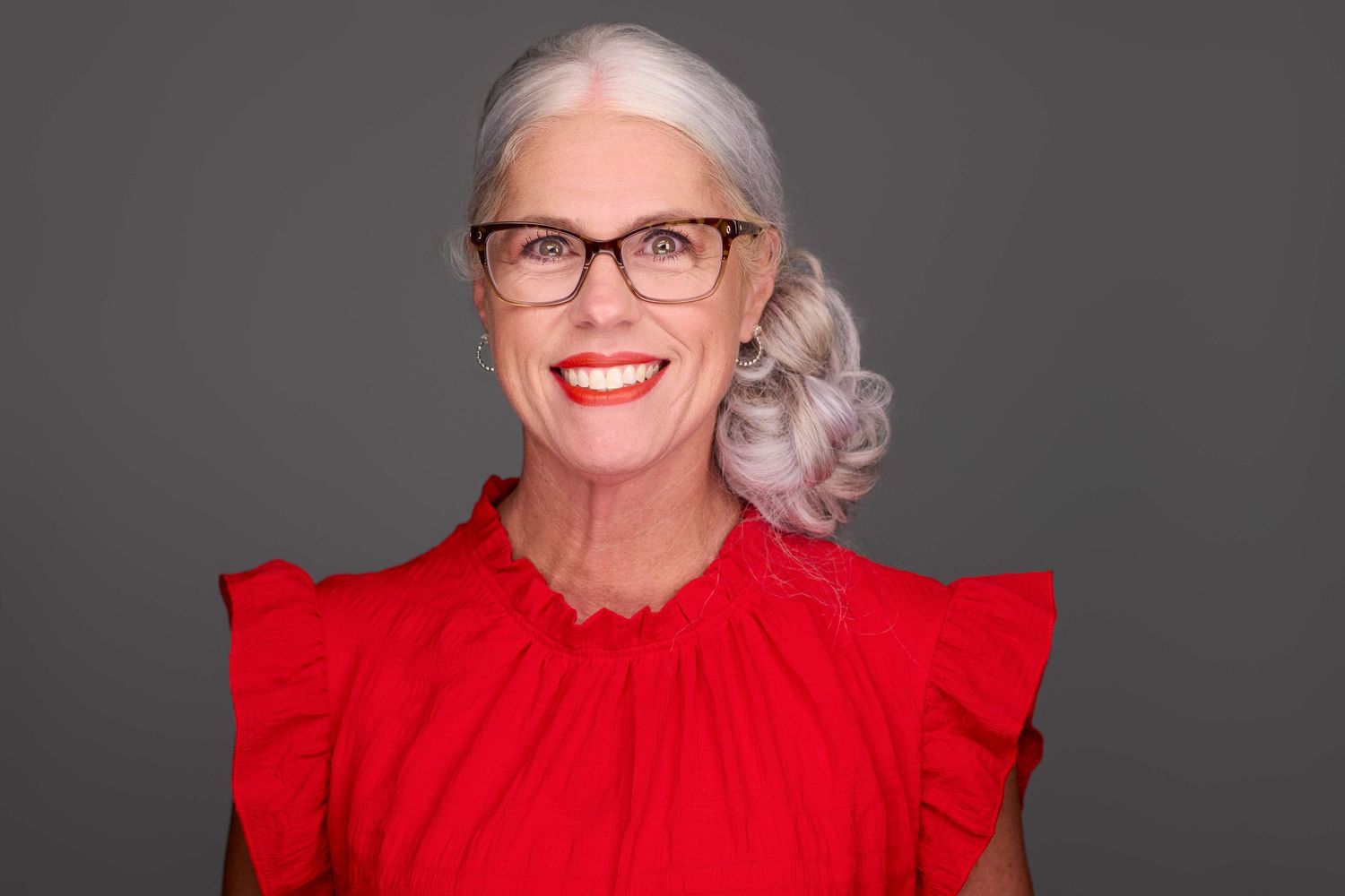Elegant headshot of person in red ruffled top against dark background.
