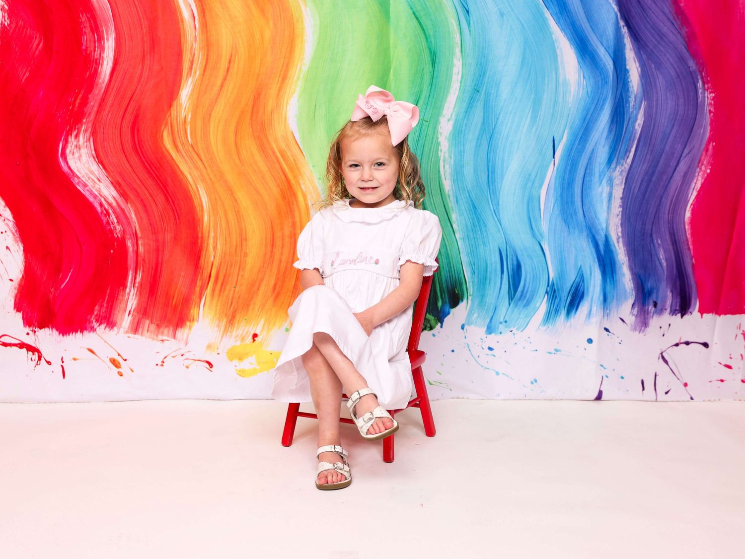 Rainbow painted backdrop creates colorful setting for children's portrait photography.