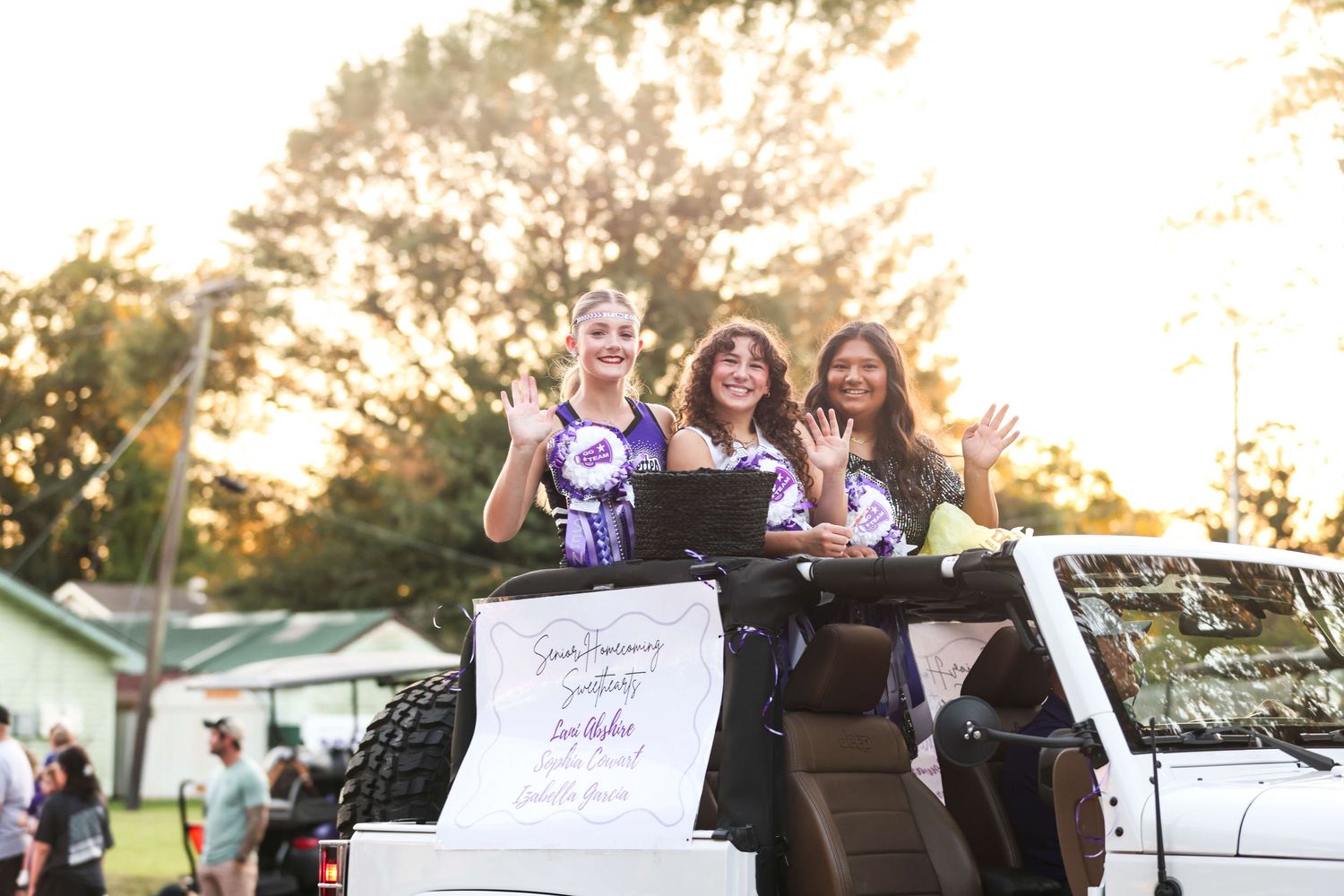 Students celebrate from the back of a decorated car during a sunset graduation parade.