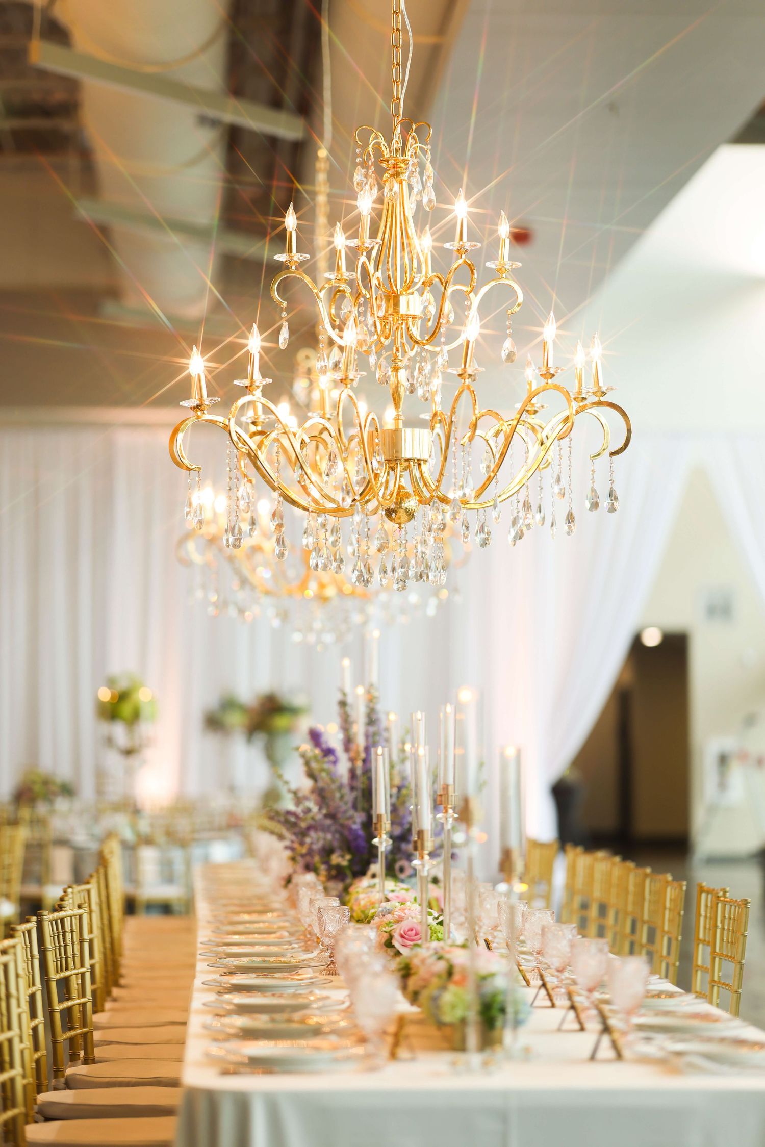 Elegant wedding reception tables with gold chandeliers and white linens create a luxurious banquet setting.