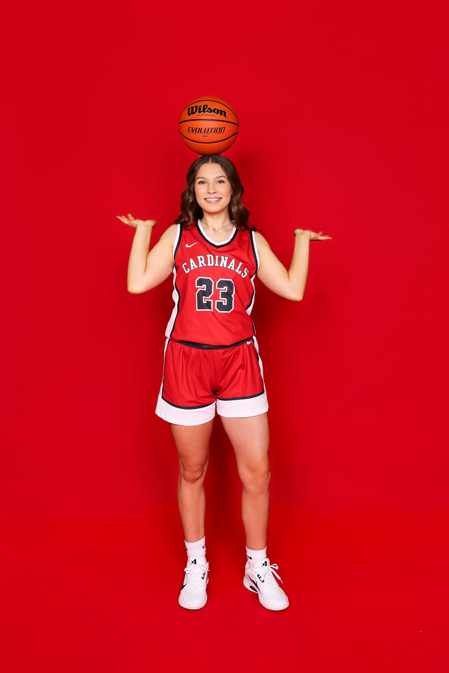 Basketball player in red Cardinals uniform poses with ball against bright red background.