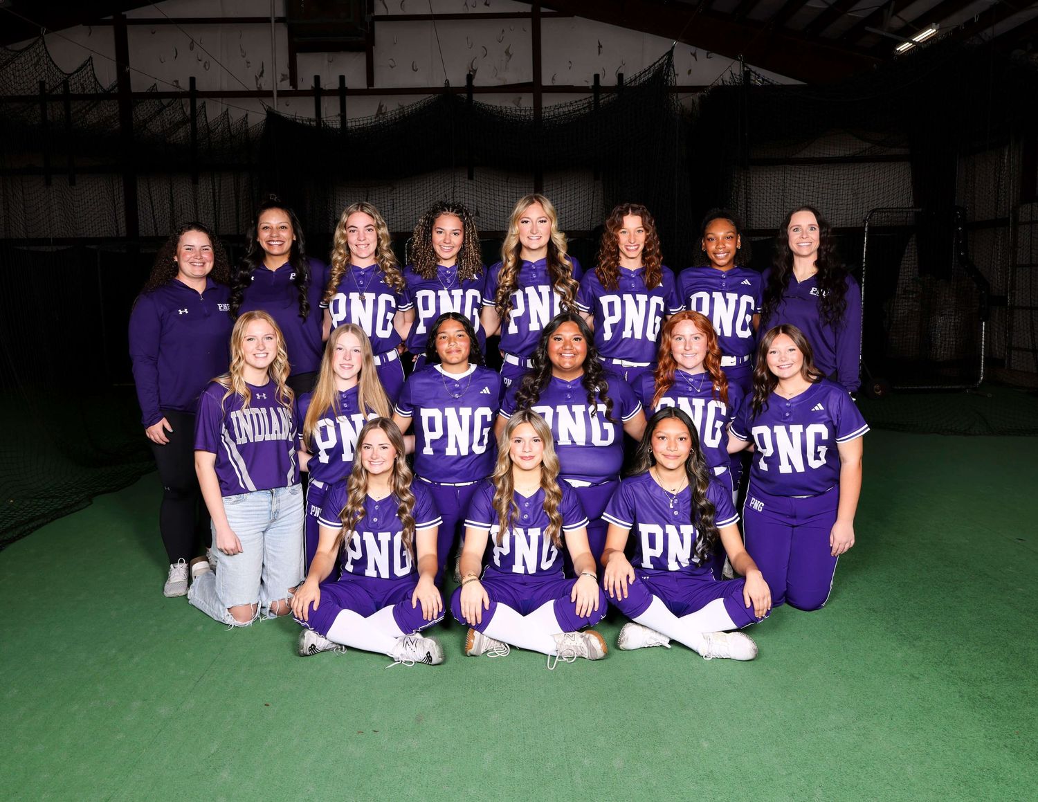 Girls basketball team in purple uniforms poses for group photo on indoor field.