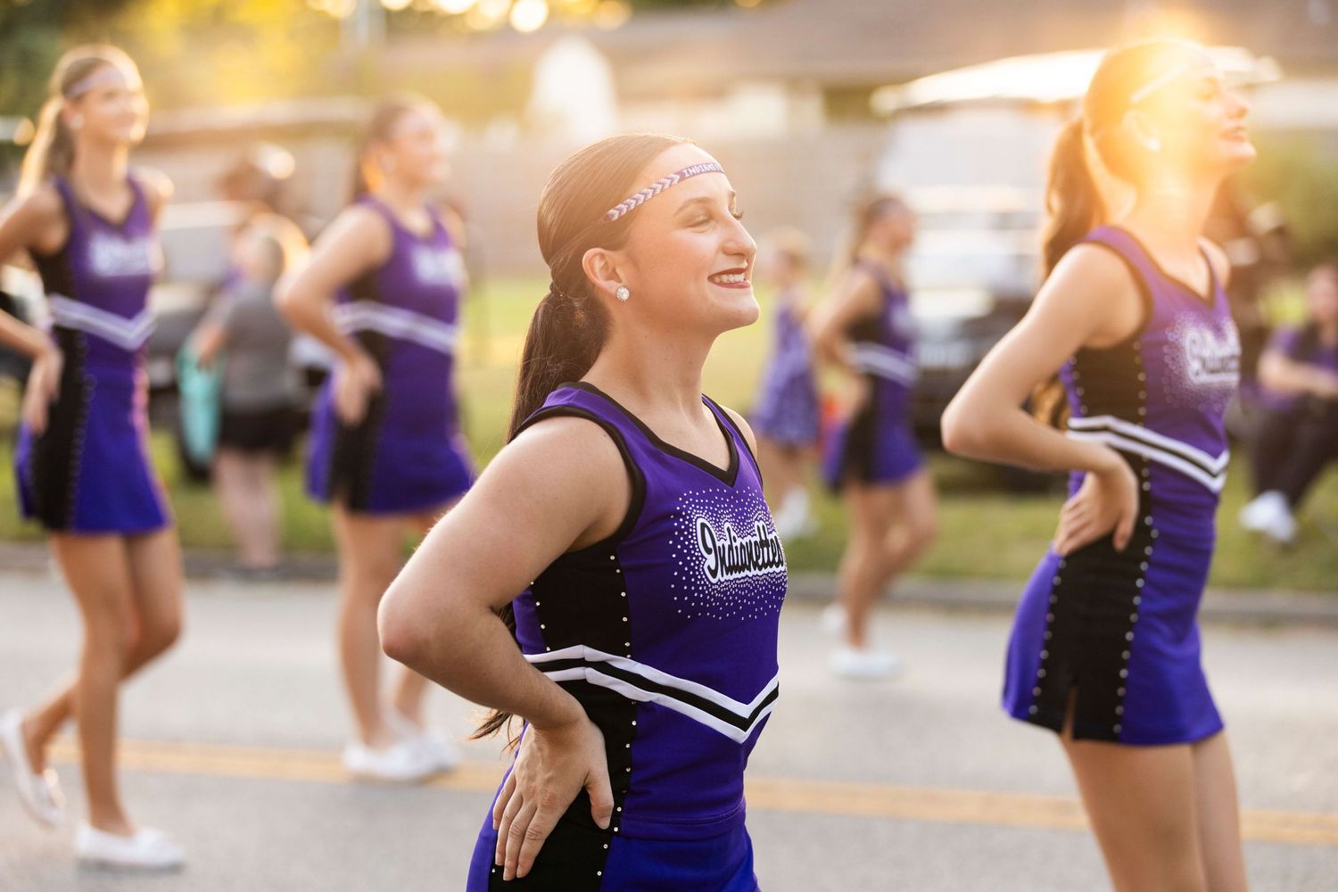 A group of cheerleaders in purple uniforms performing a dance routine outdoors during sunset.