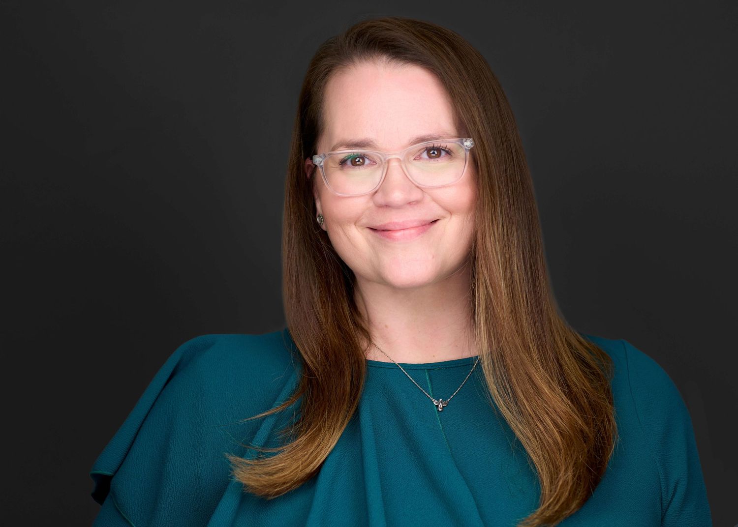 Professional headshot of person in teal blouse against dark background.