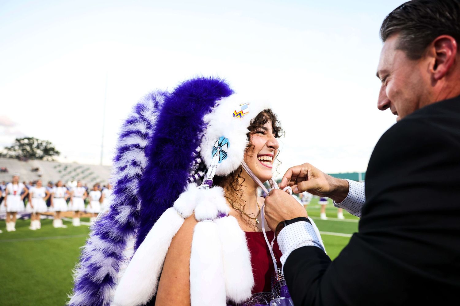 A group of people celebrate at an outdoor wedding ceremony with purple feather decorations.