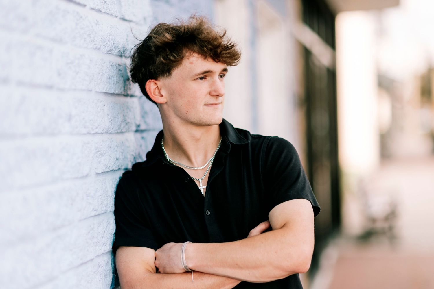 Person in black shirt poses against white brick wall in urban setting.