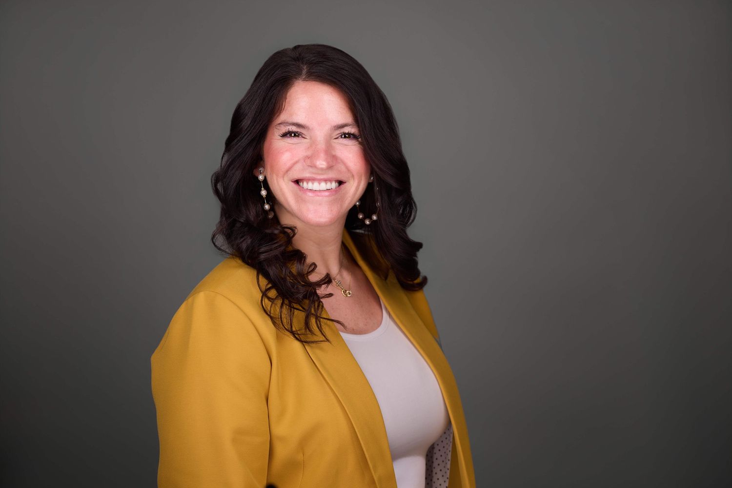 Professional headshot of person wearing bright yellow blazer with natural smile.