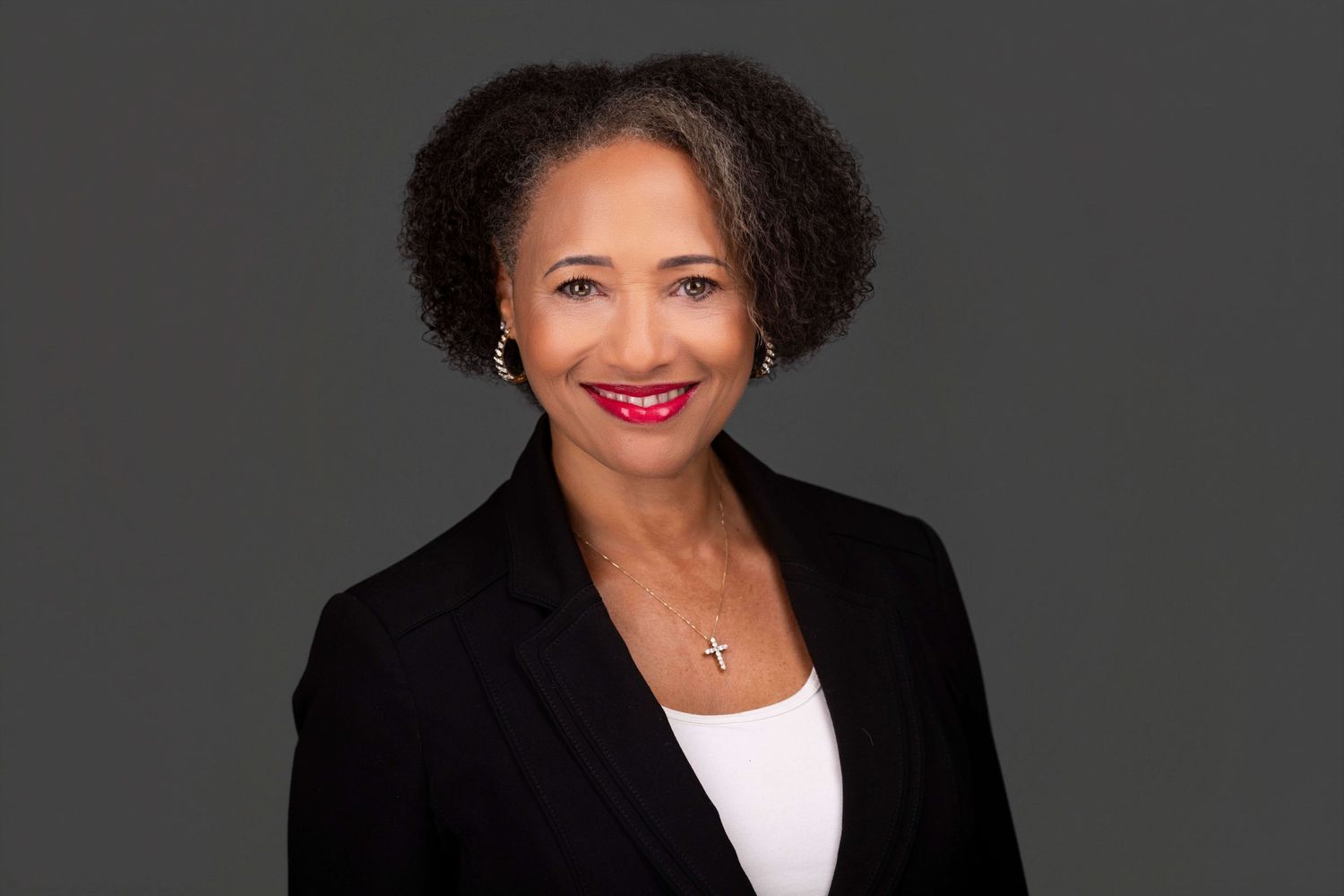Professional headshot of person in black attire against dark background with warm smile.