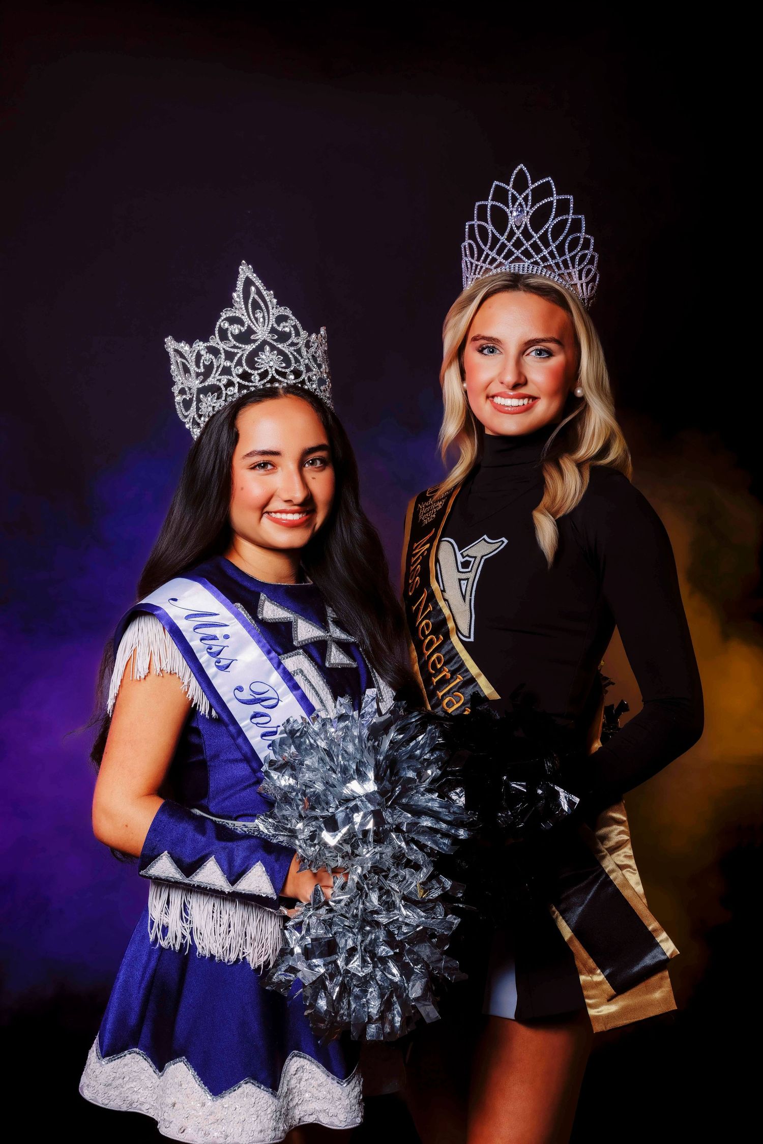 Two pageant winners in sparkling crowns and dresses pose together with pom poms.