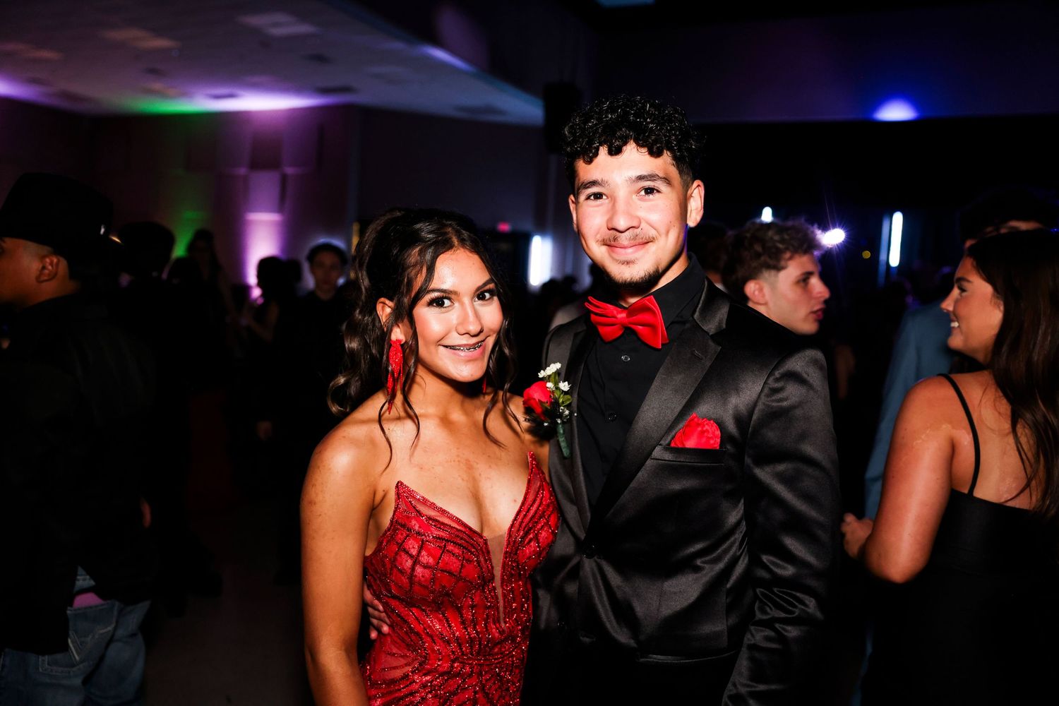 People dance and socialize at a dimly lit formal event with red and black attire.