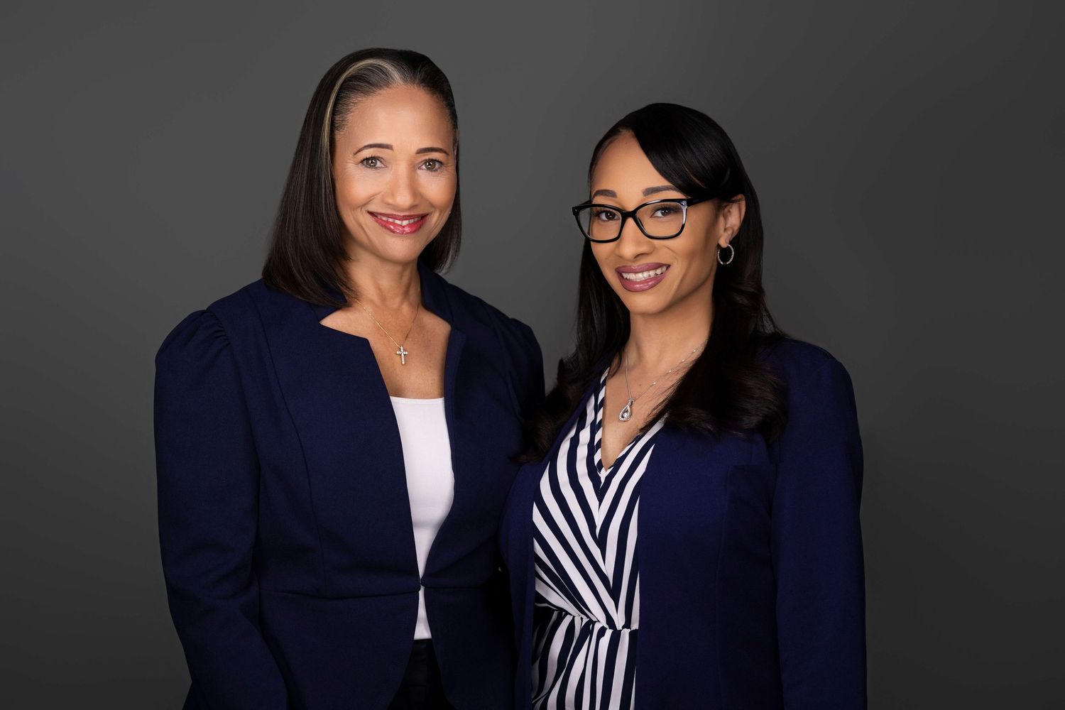 Professional portrait of two people in navy blazers against dark background.