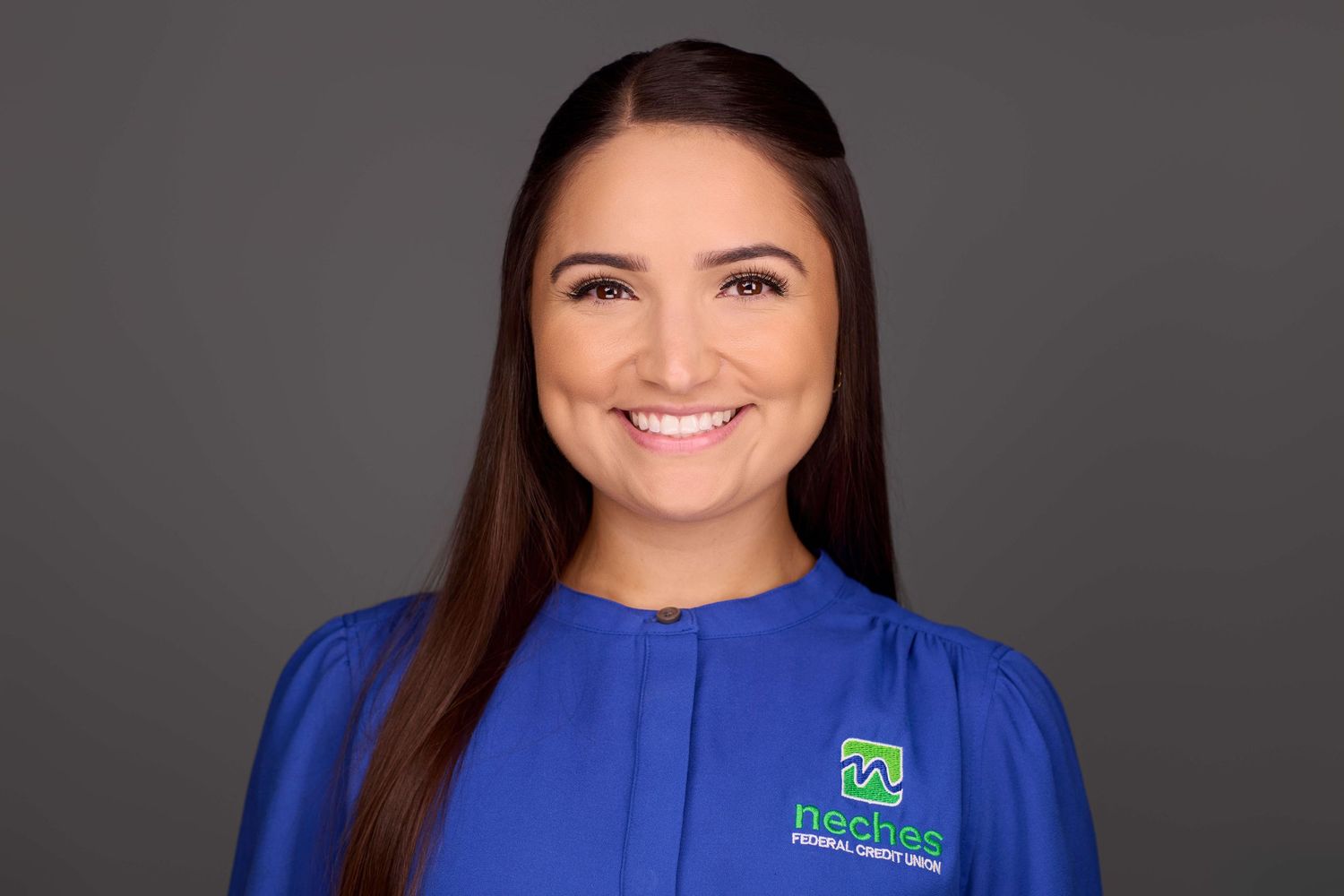 Professional headshot of someone in a royal blue top with a company logo against a dark background.
