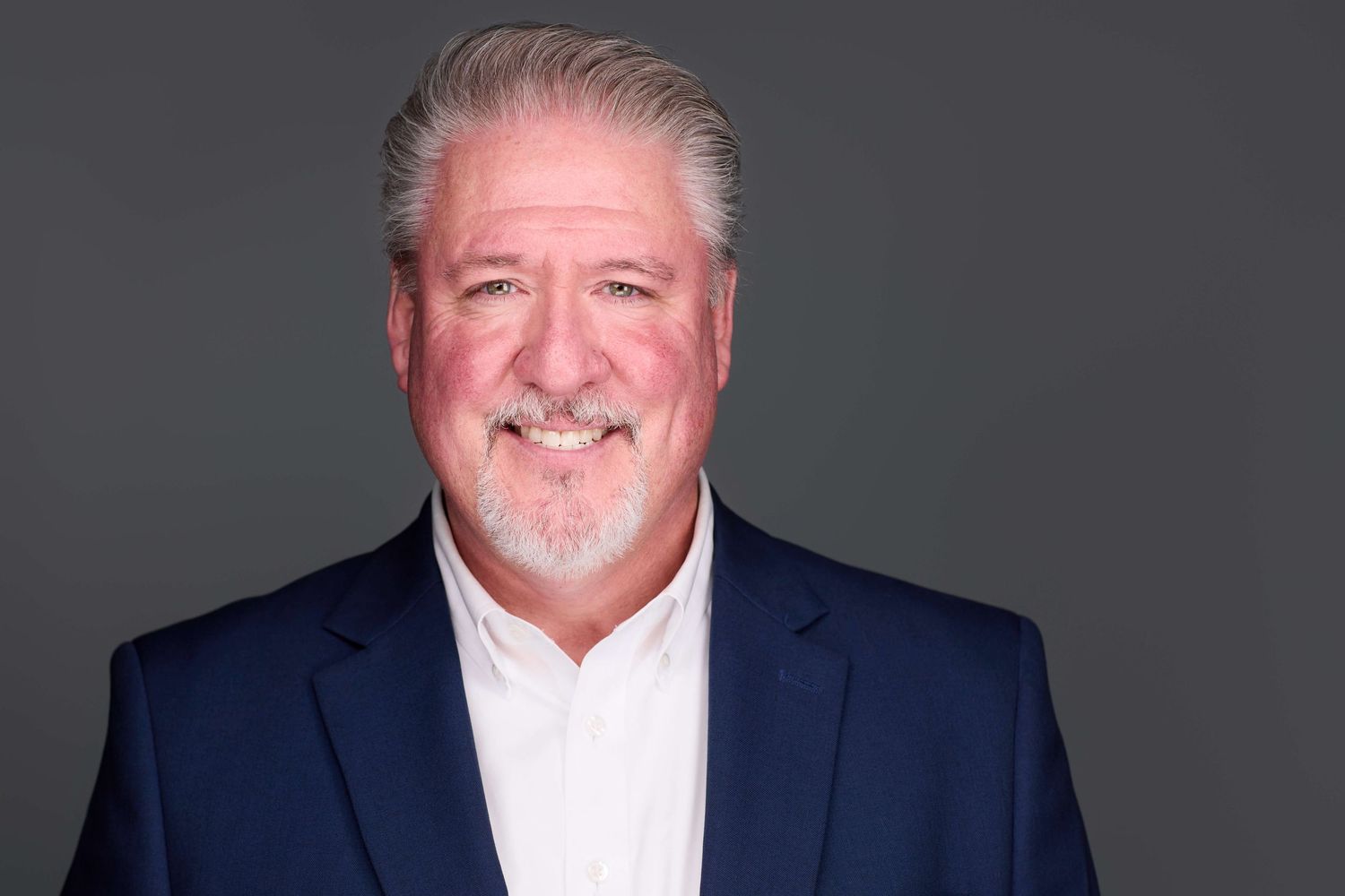 Professional headshot of person in navy suit against dark gray background.