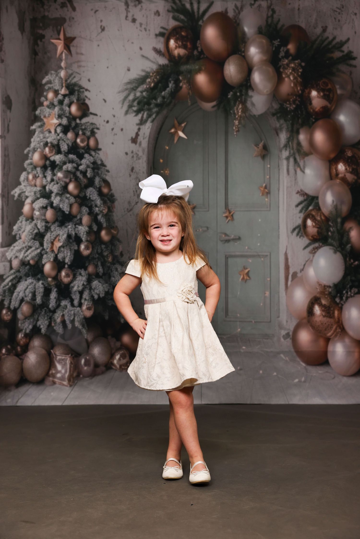 A child in a cream colored dress twirls and poses in front of a Christmas themed backdrop.