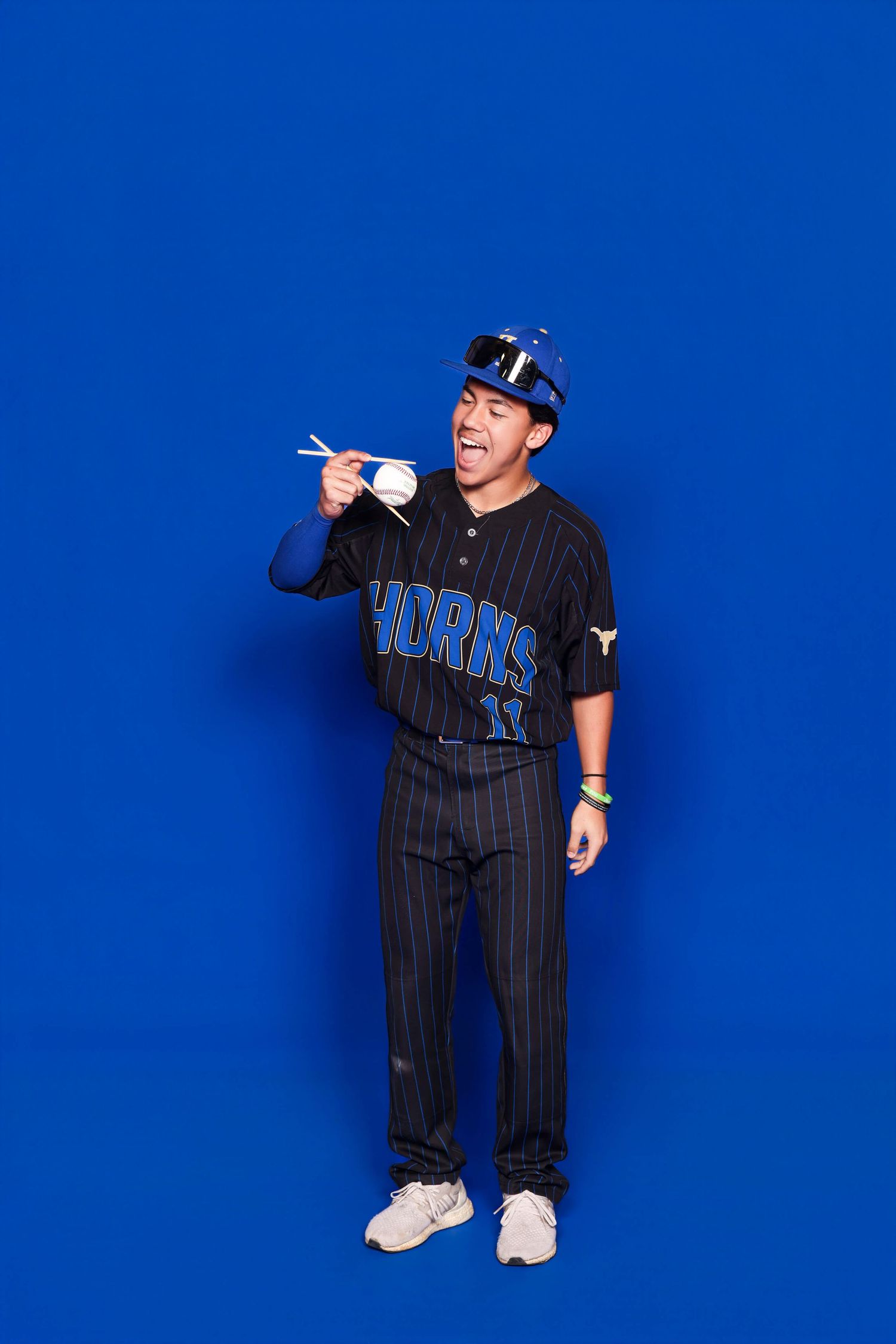 Baseball player in pinstripe uniform poses playfully against bright blue backdrop during photo shoot.