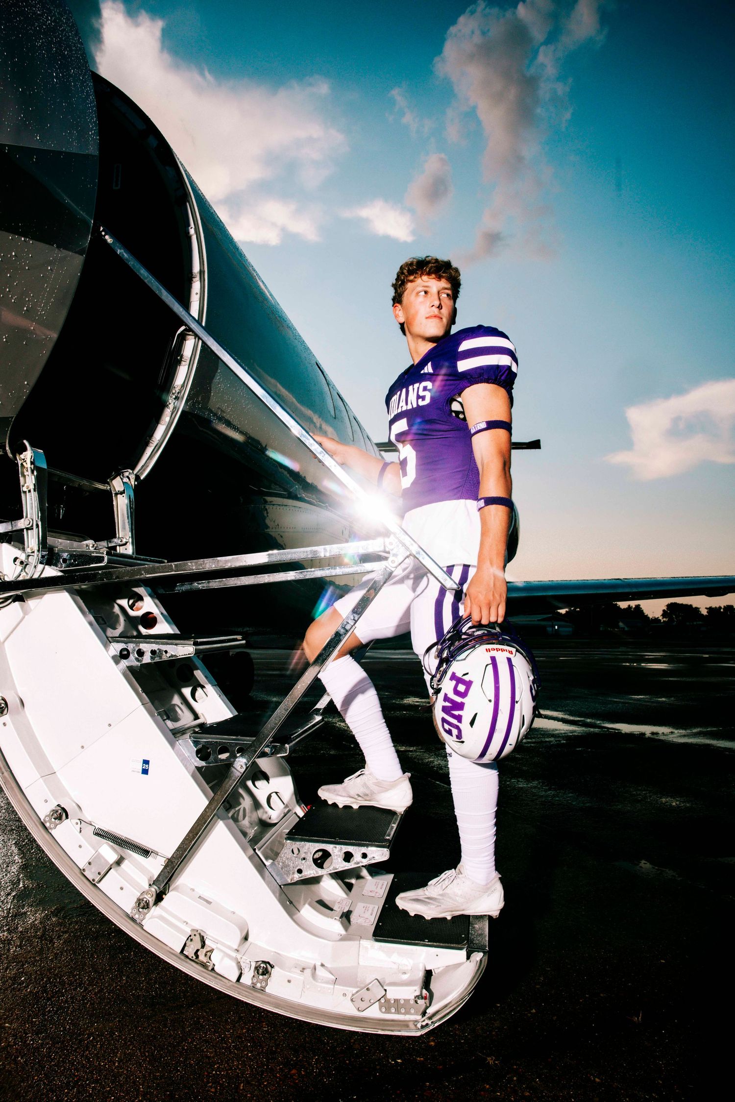 Football player in purple uniform sitting on metal bleachers during sunset.