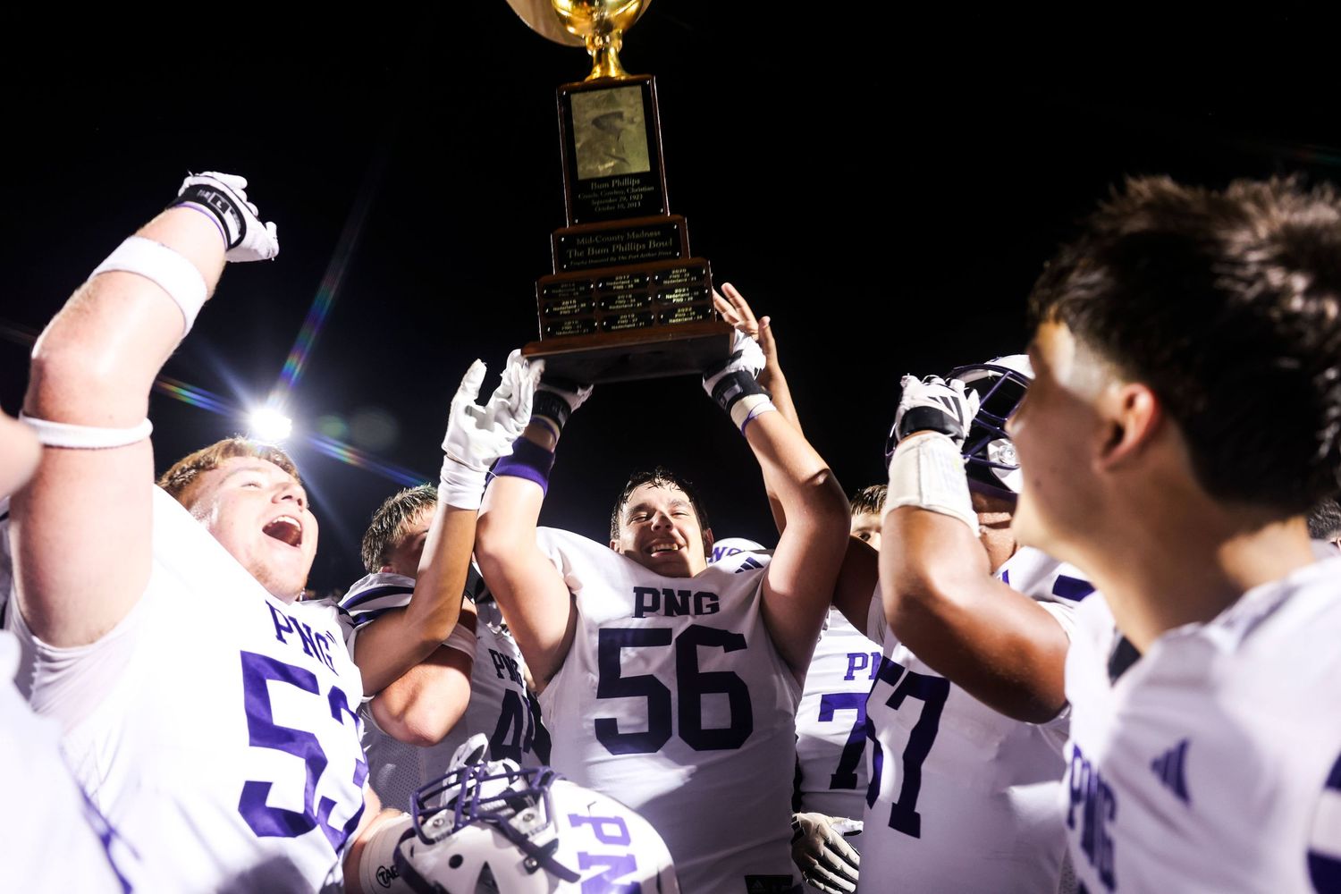 Football team celebrates victory by hoisting championship trophy under stadium lights.